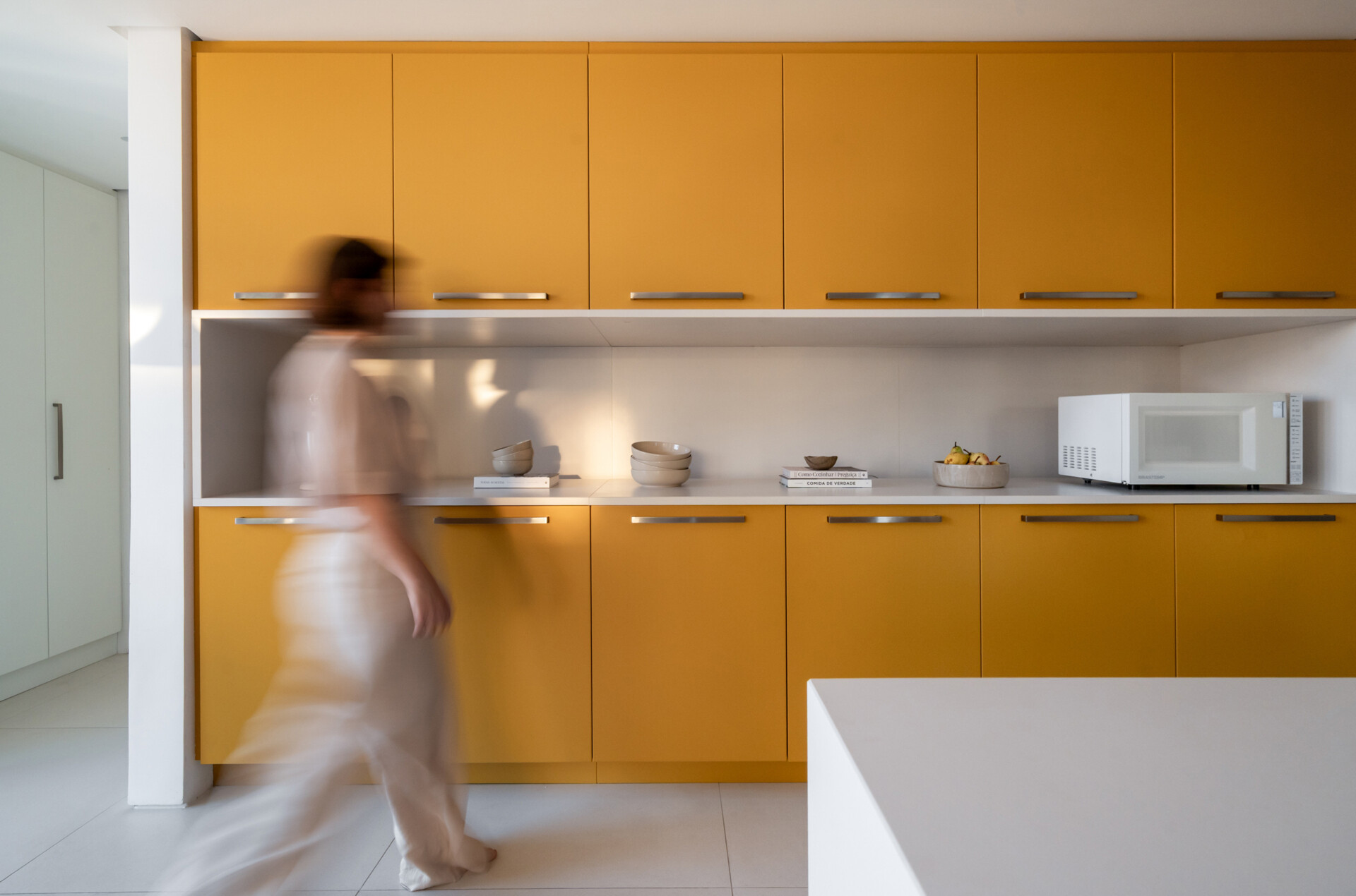 Behind warm timber panels is a cheerful kitchen where pale cabinetry meets bold mustard-yellow storage.