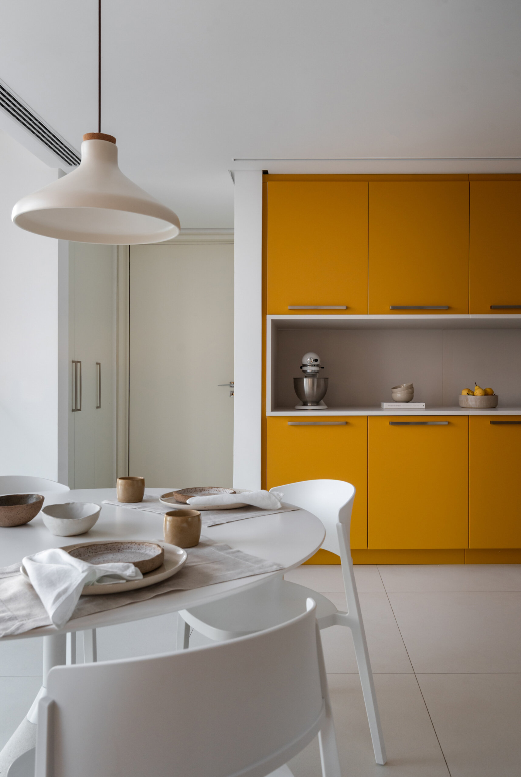 Behind warm timber panels is a cheerful kitchen where pale cabinetry meets bold mustard-yellow storage.