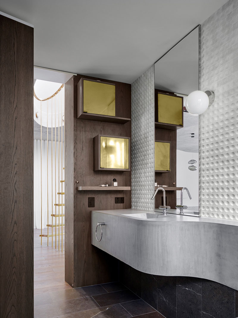 A concealed powder room sits behind a pivoting bookcase, featuring a sculptural curved concrete basin, bench and dark timber wall.