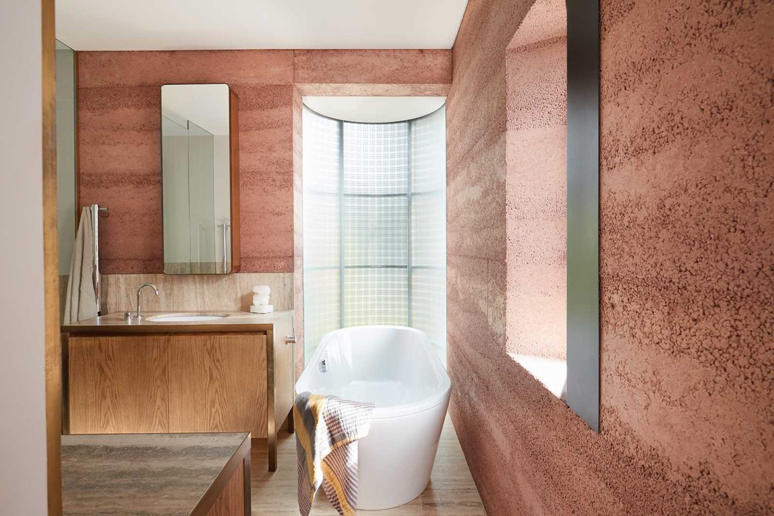 Rammed earth walls and curved windows bring earthy textures and unusual architectural details into one of the bathrooms at Earth-Ship in Sydney.