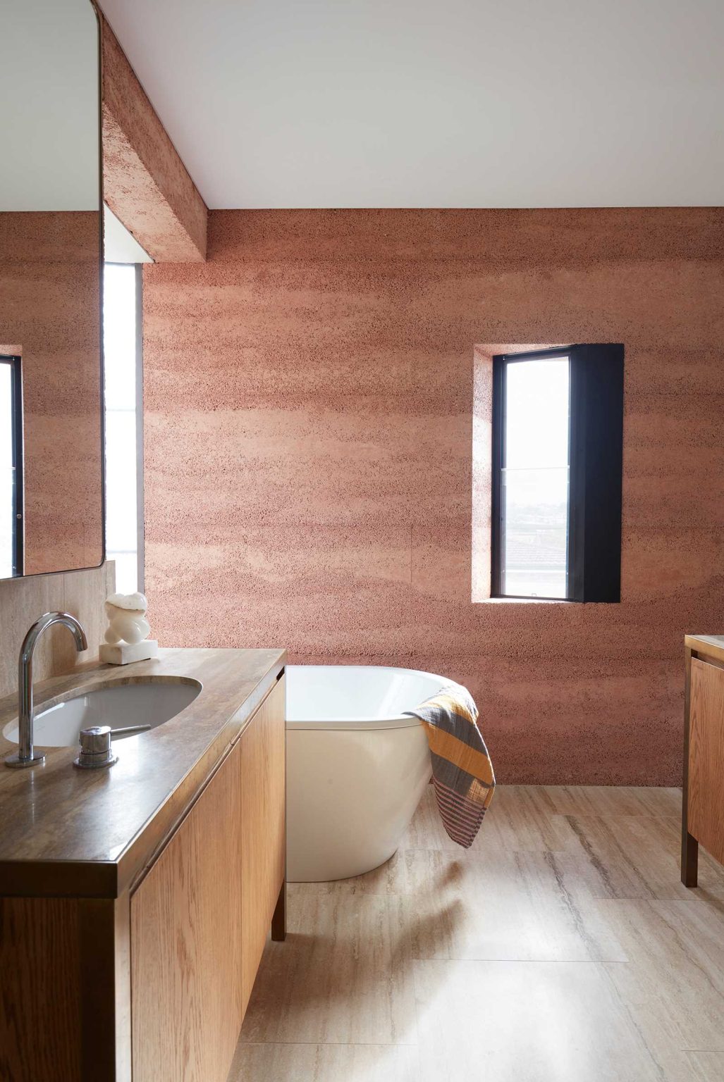 Rammed earth walls and curved windows bring earthy textures and unusual architectural details into one of the bathrooms at Earth-Ship in Sydney.