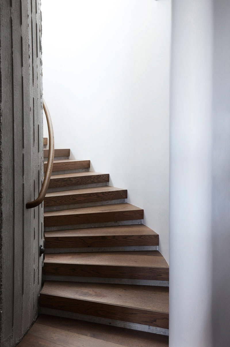 An elliptical concrete stairwell with warm oak treads forms the vertical centre of The Books House, combining curved architecture with tactile natural materials.