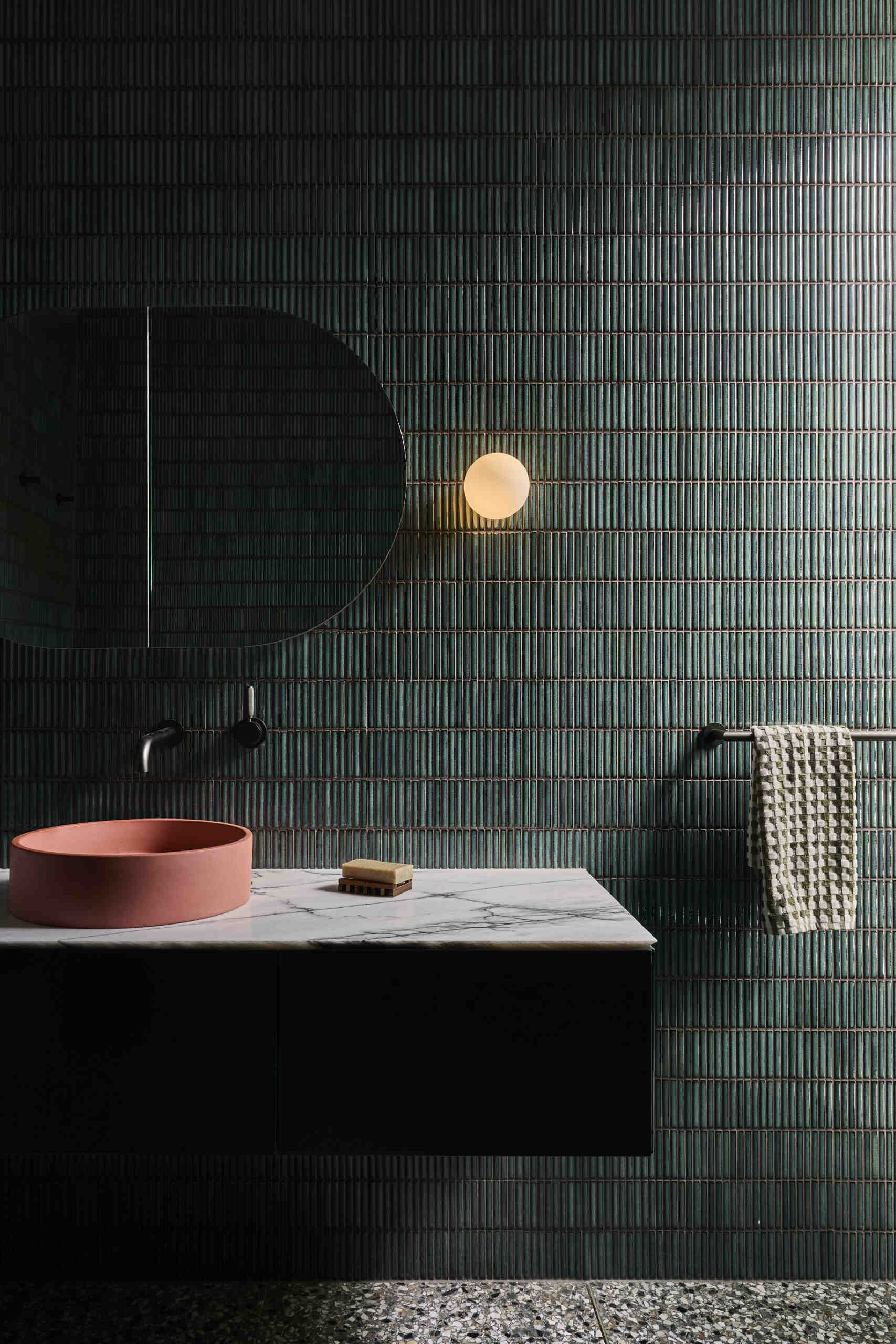 See inside this colourful guest bathroom at Sasso Nero, featuring deep green vertical tiles, a floating black vanity, veined marble, a muted terracotta vessel sink and a softly glowing globe wall light.