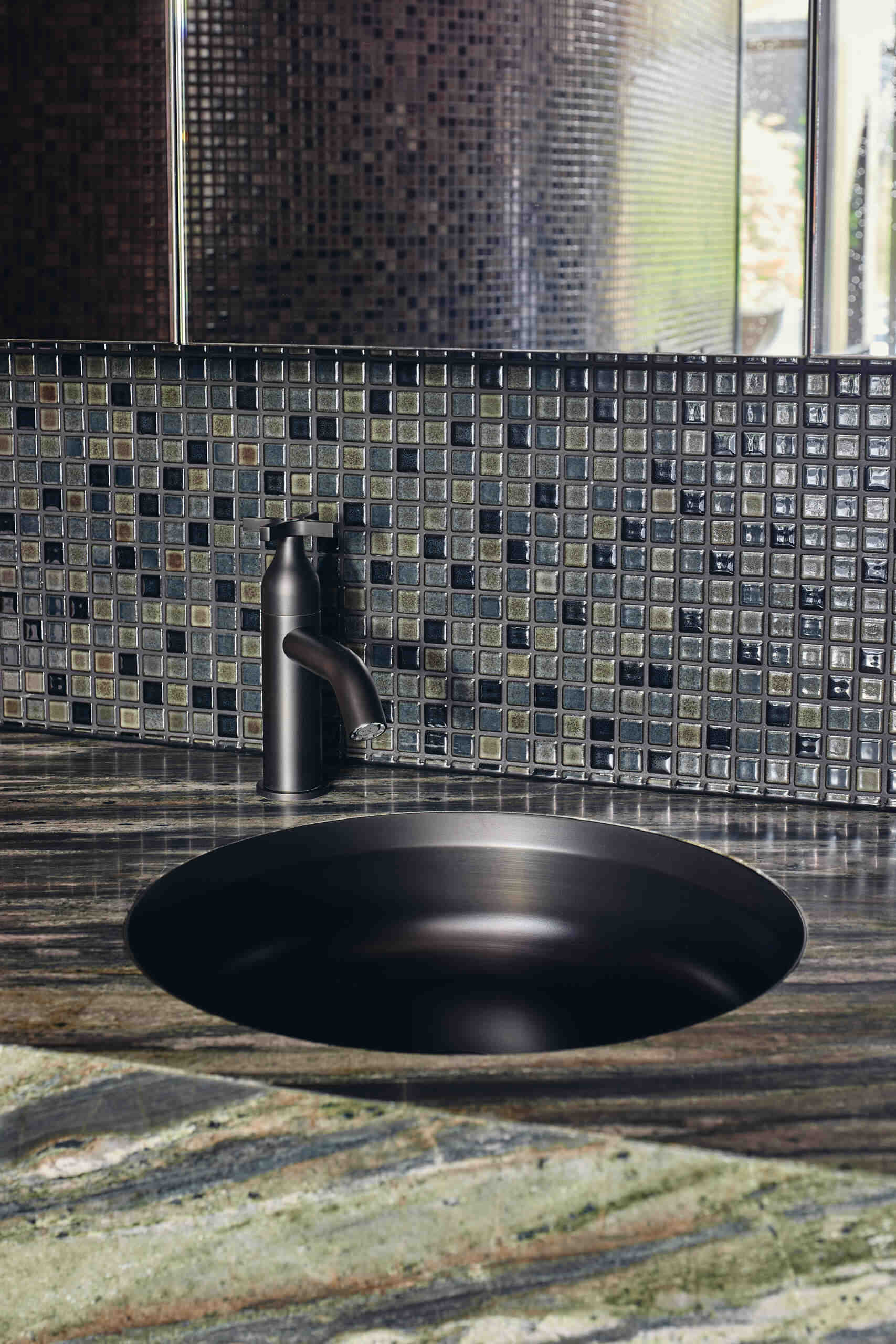 A primary bathroom combines warm wood paneling, dark mosaic tiles and richly veined green stone, with expansive garden views, a sculptural freestanding bath and adjoining dressing area.