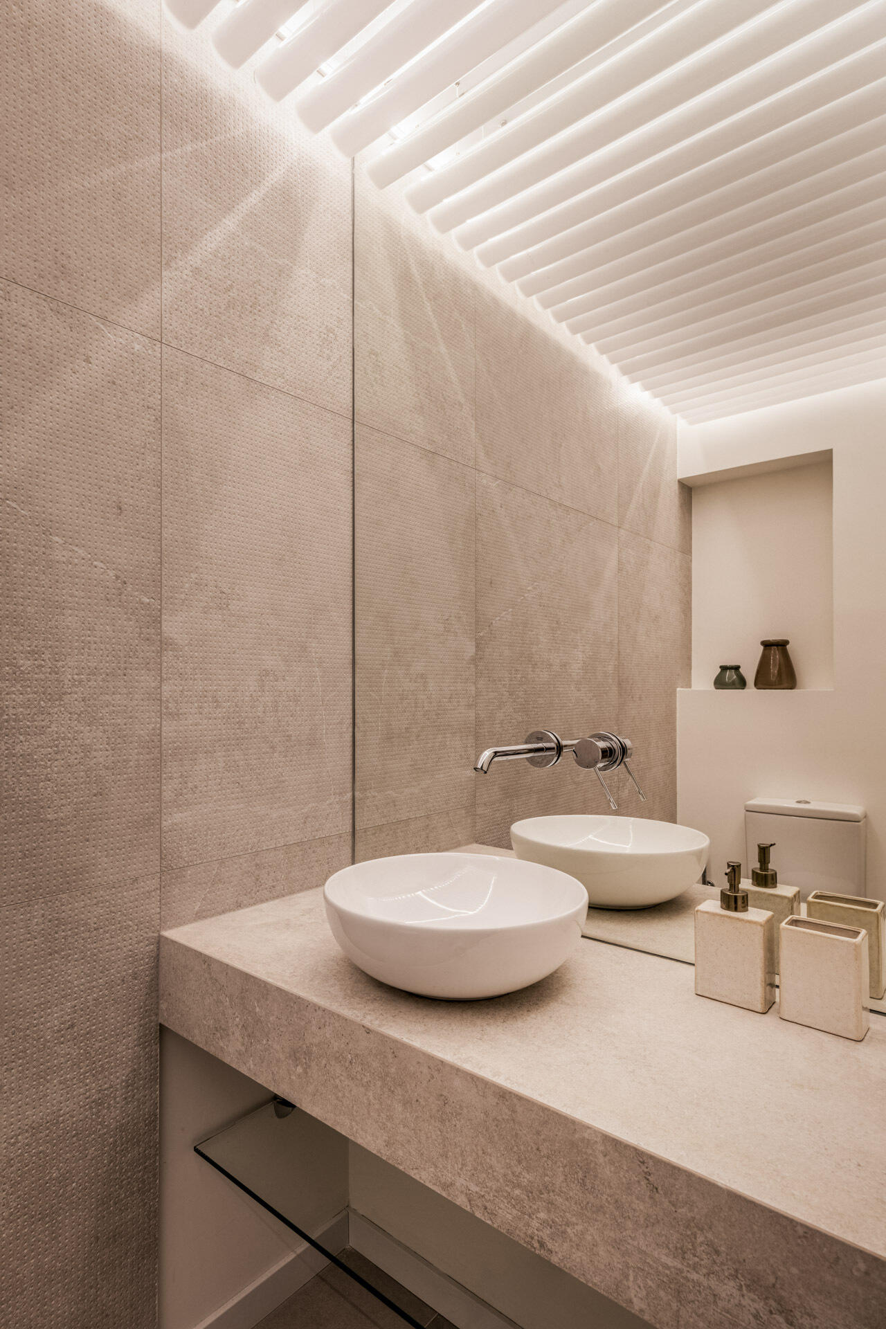 A sculptural powder room inside the central timber volume features curved backlit slats, sand-toned textured walls and an organic freestanding basin.