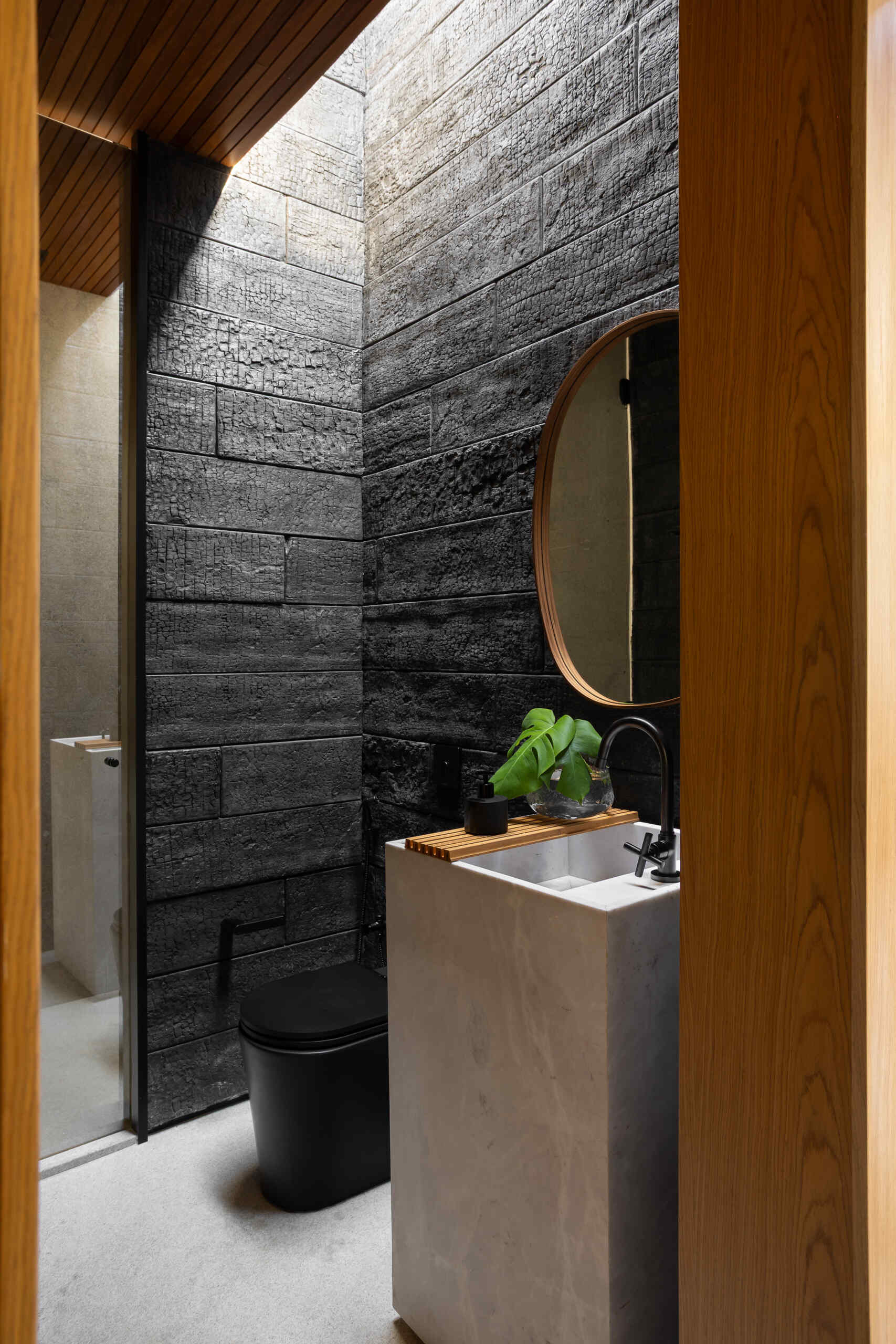 Charred black walls, warm wood framing and a pale stone sink create a textured powder room at Casa da Mata, with daylight from above revealing the surface and restrained black fixtures completing the design.