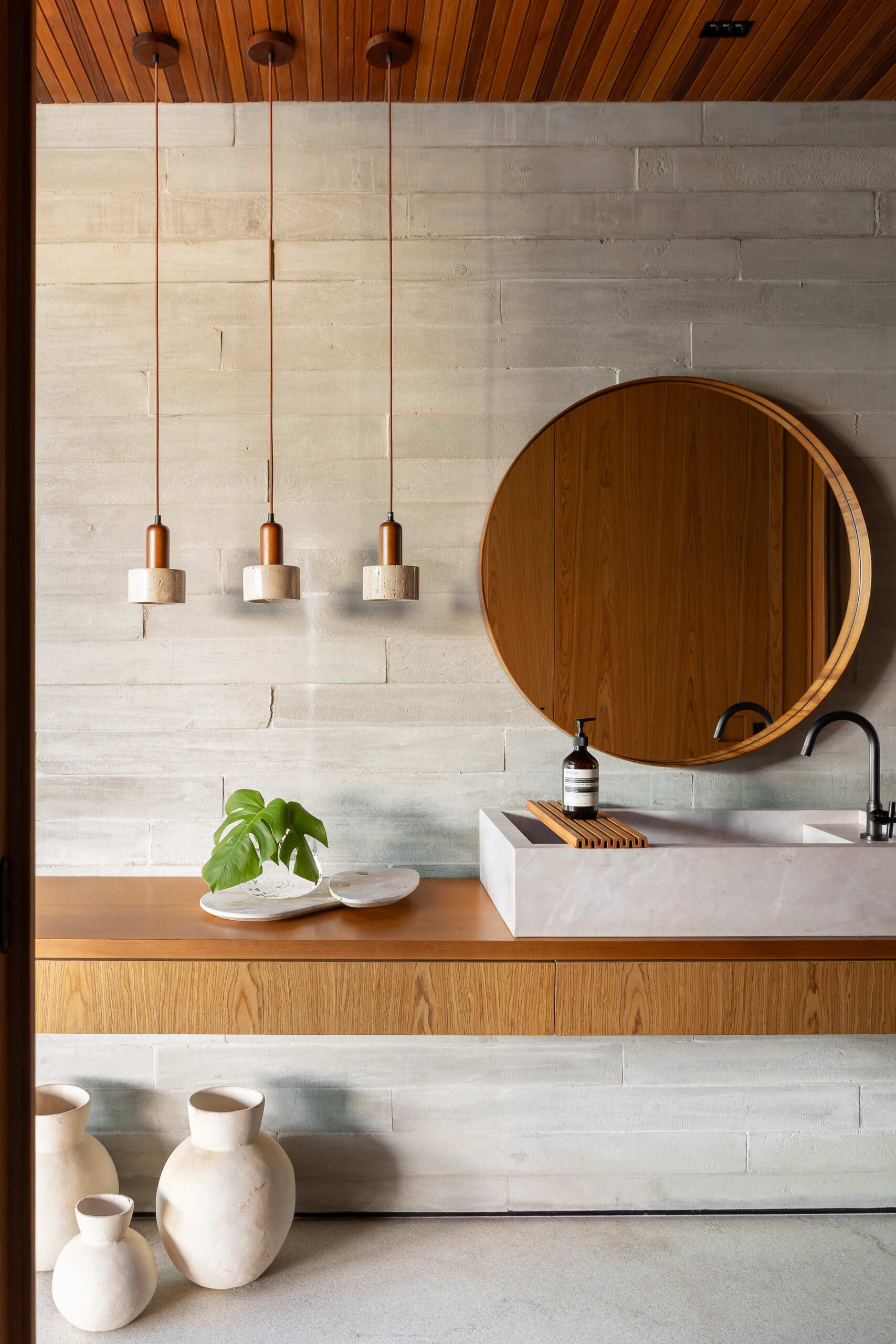 Near the wine cellar, warm wood and textured gray masonry frame a compact vanity area, while a glass-fronted wine cellar adds depth and visual interest to the passage.
