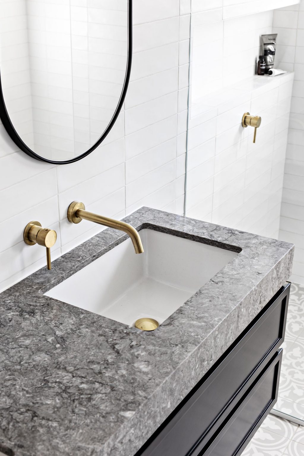 Tour the hidden ensuite behind the custom wardrobe doors, featuring patterned floor tiles, a black floating vanity, grey stone, white subway tiles, brass hardware and a double shower.