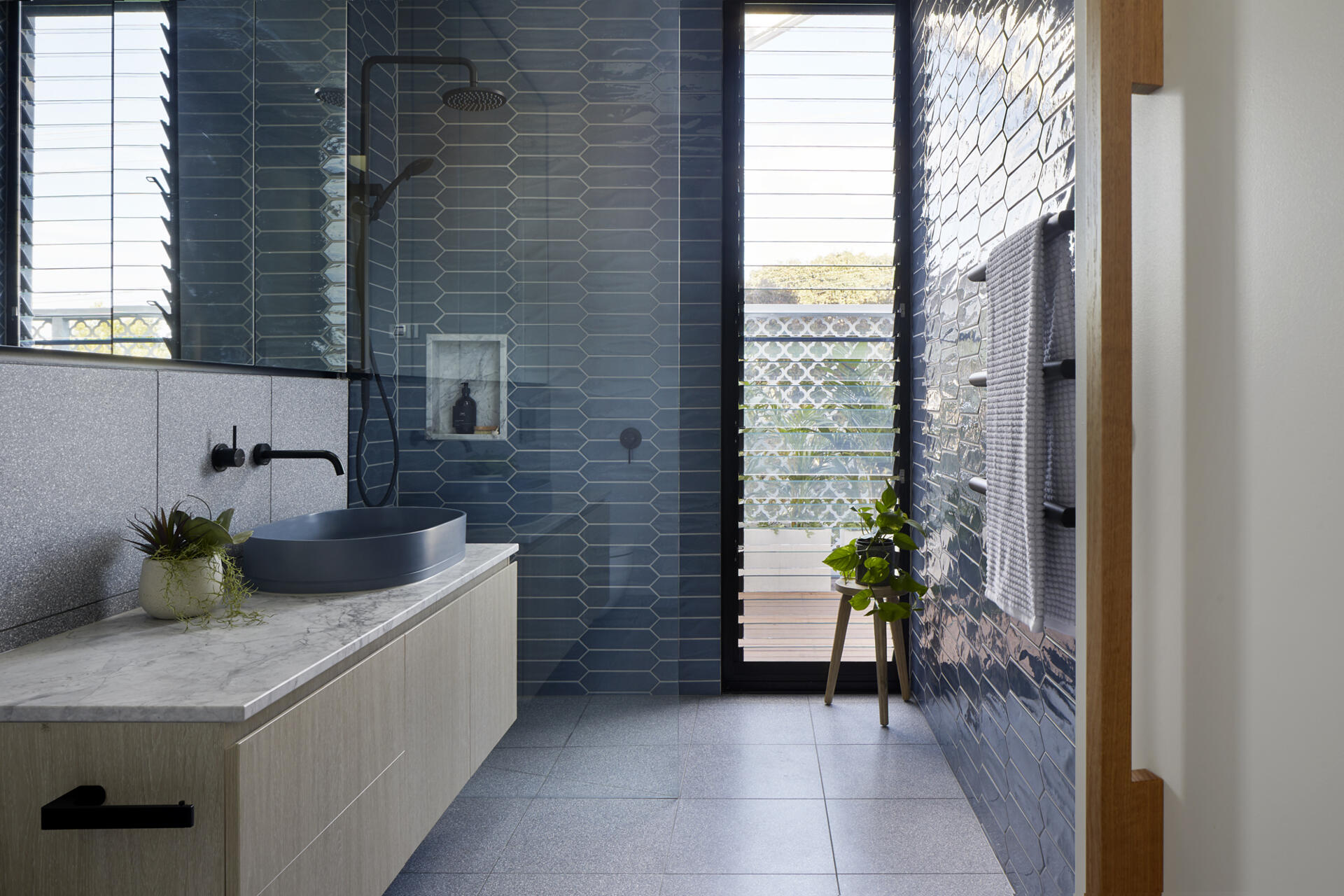 Blue picket tiles, a floating marble vanity, and built-in shower storage give this small bathroom a fresh contemporary look.