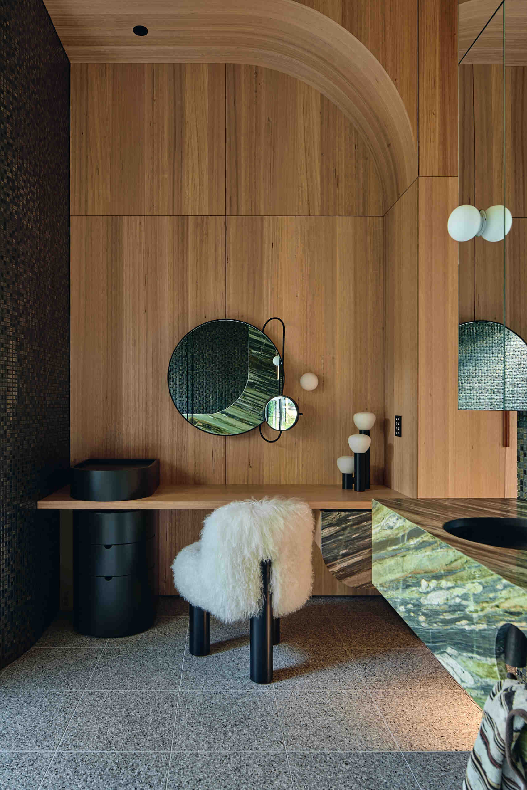 A primary bathroom combines warm wood paneling, dark mosaic tiles and richly veined green stone, with expansive garden views, a sculptural freestanding bath and adjoining dressing area.