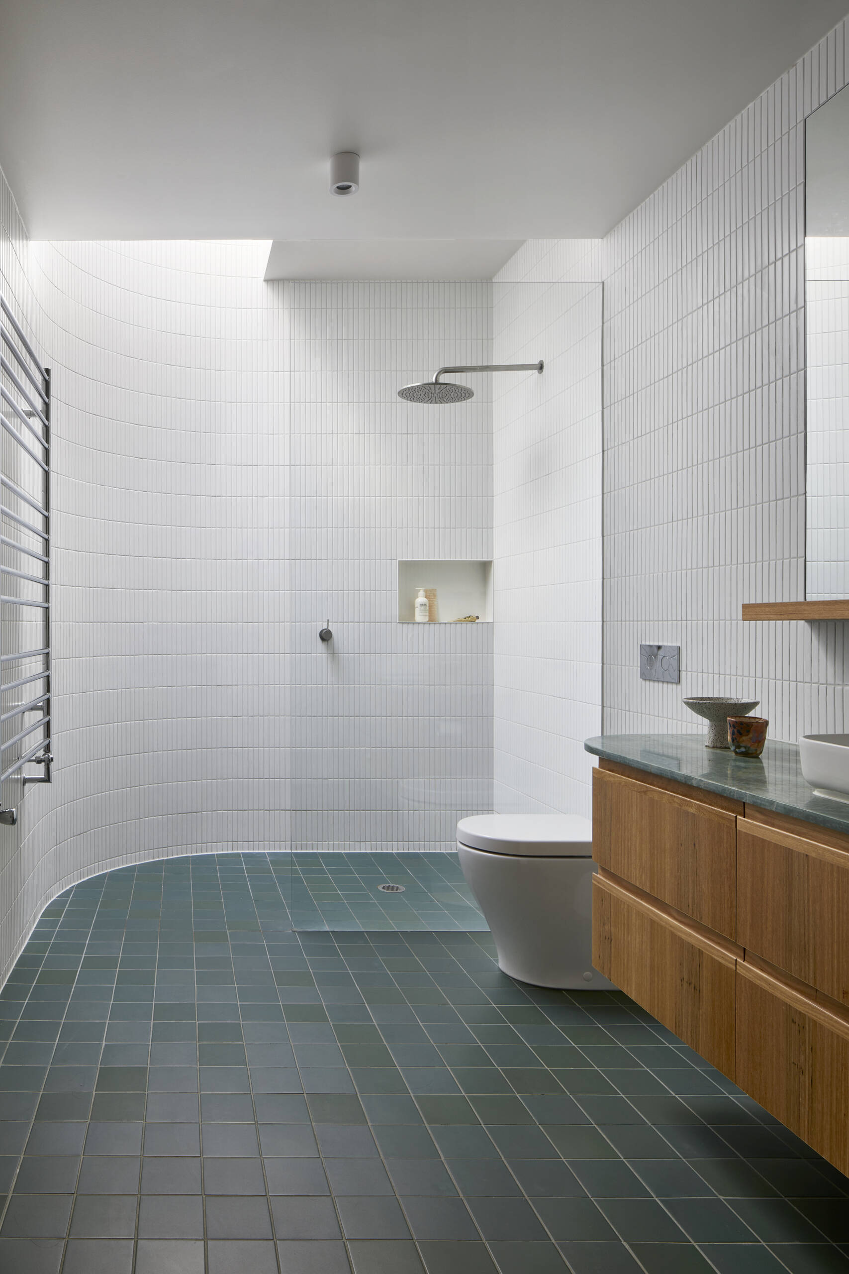 A modern white and wood bathroom with colourful floor tiles, a green marble countertop, and a skylight in the shower.