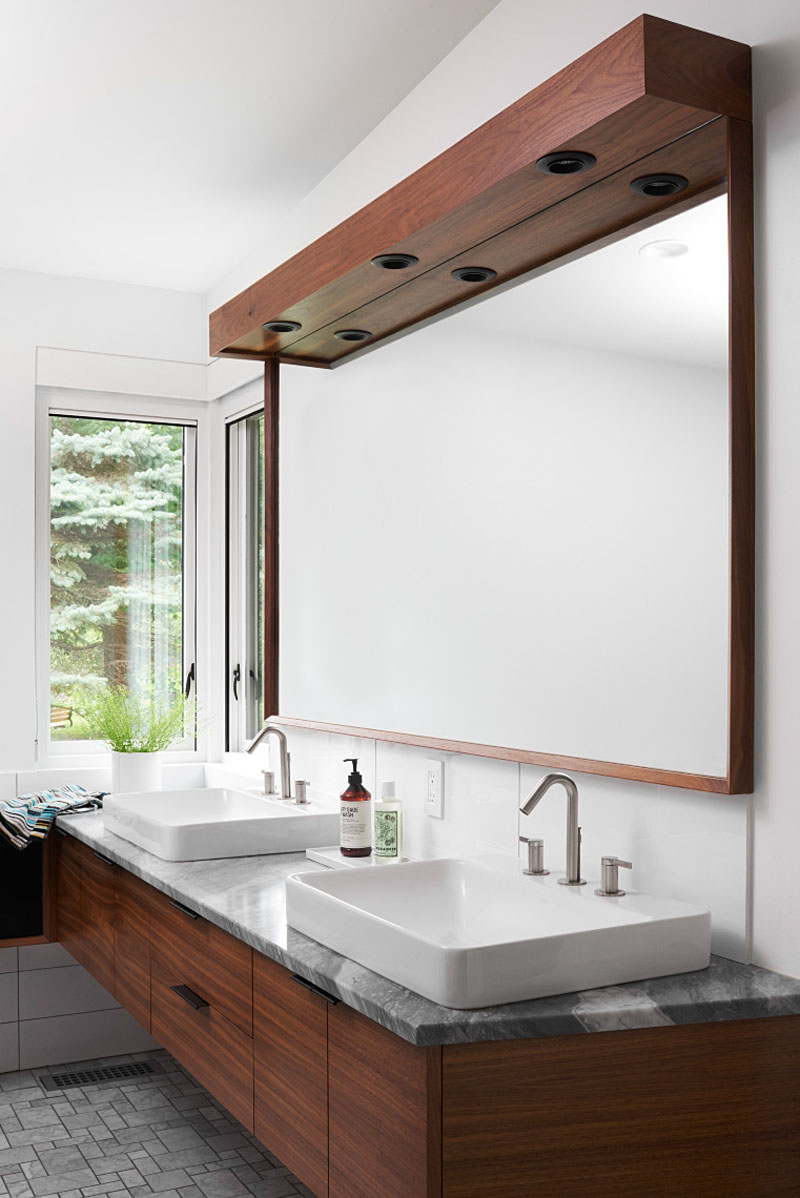 A dark wood-framed mirror, dual-sink vanity and stone counter create a warm, understated master bathroom in this Minneapolis home.