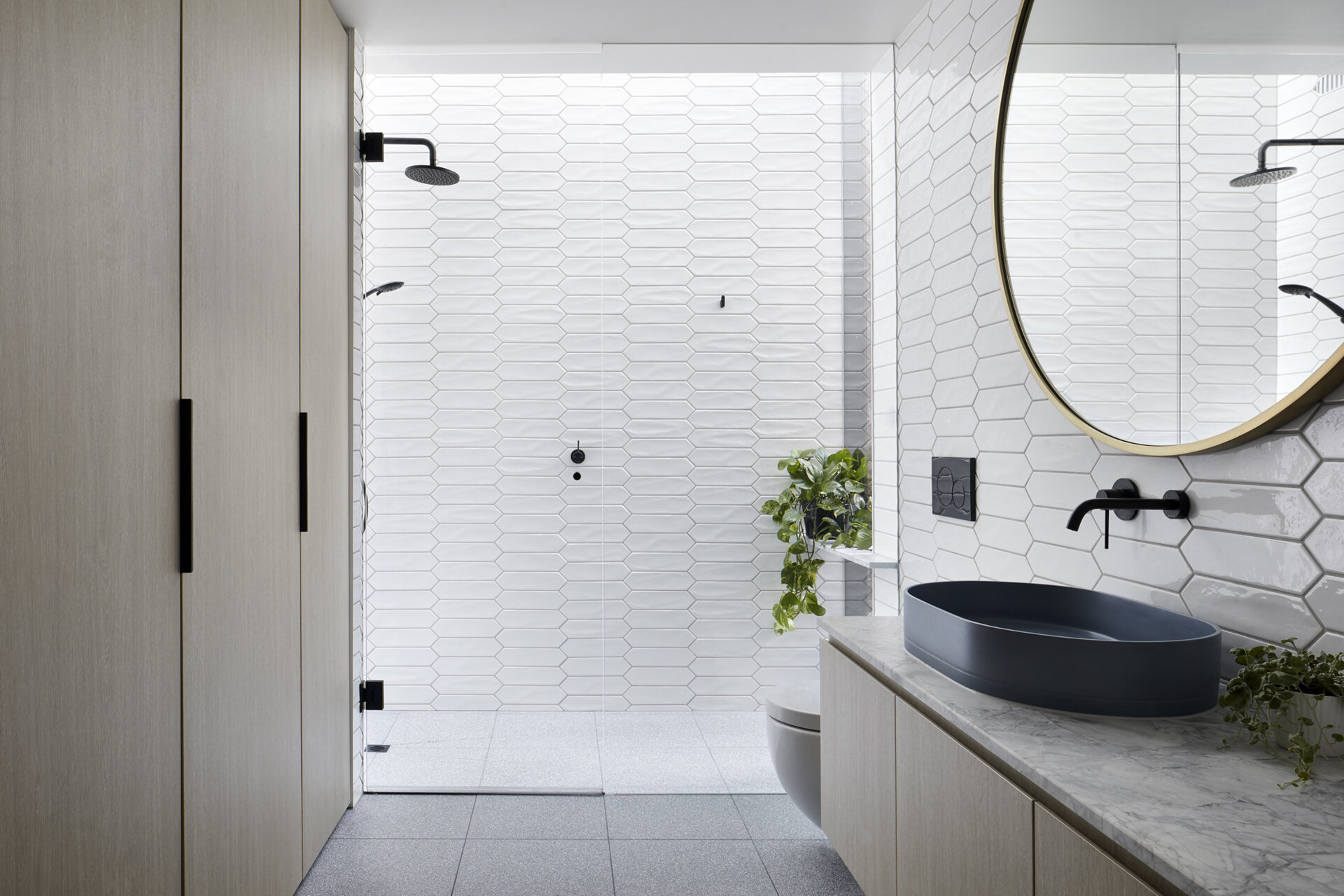 White picket tiles, hidden laundry storage, and a shower overlooking a tiny garden make this compact bathroom feel beautifully open.