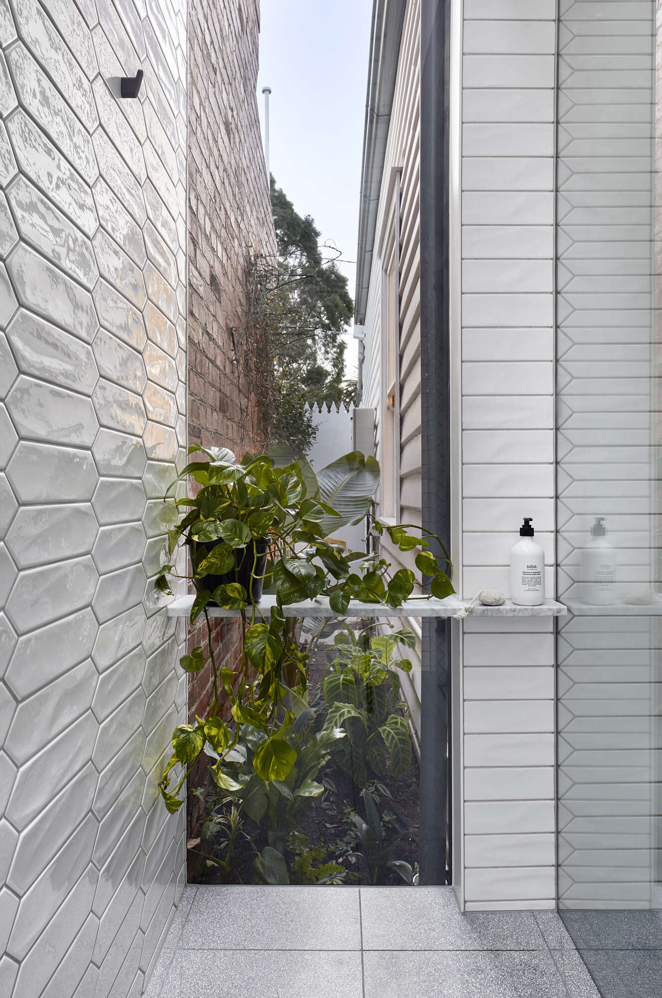 White picket tiles, hidden laundry storage, and a shower overlooking a tiny garden make this compact bathroom feel beautifully open.