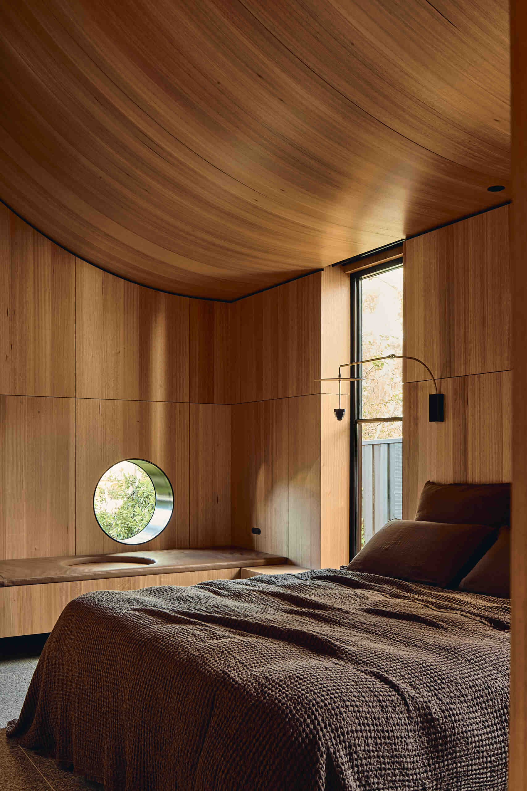 The primary suite at Babylonia features a cocoon-like bedroom, timber-lined ceilings, natural stone and views toward the garden beneath the eucalypt canopy.