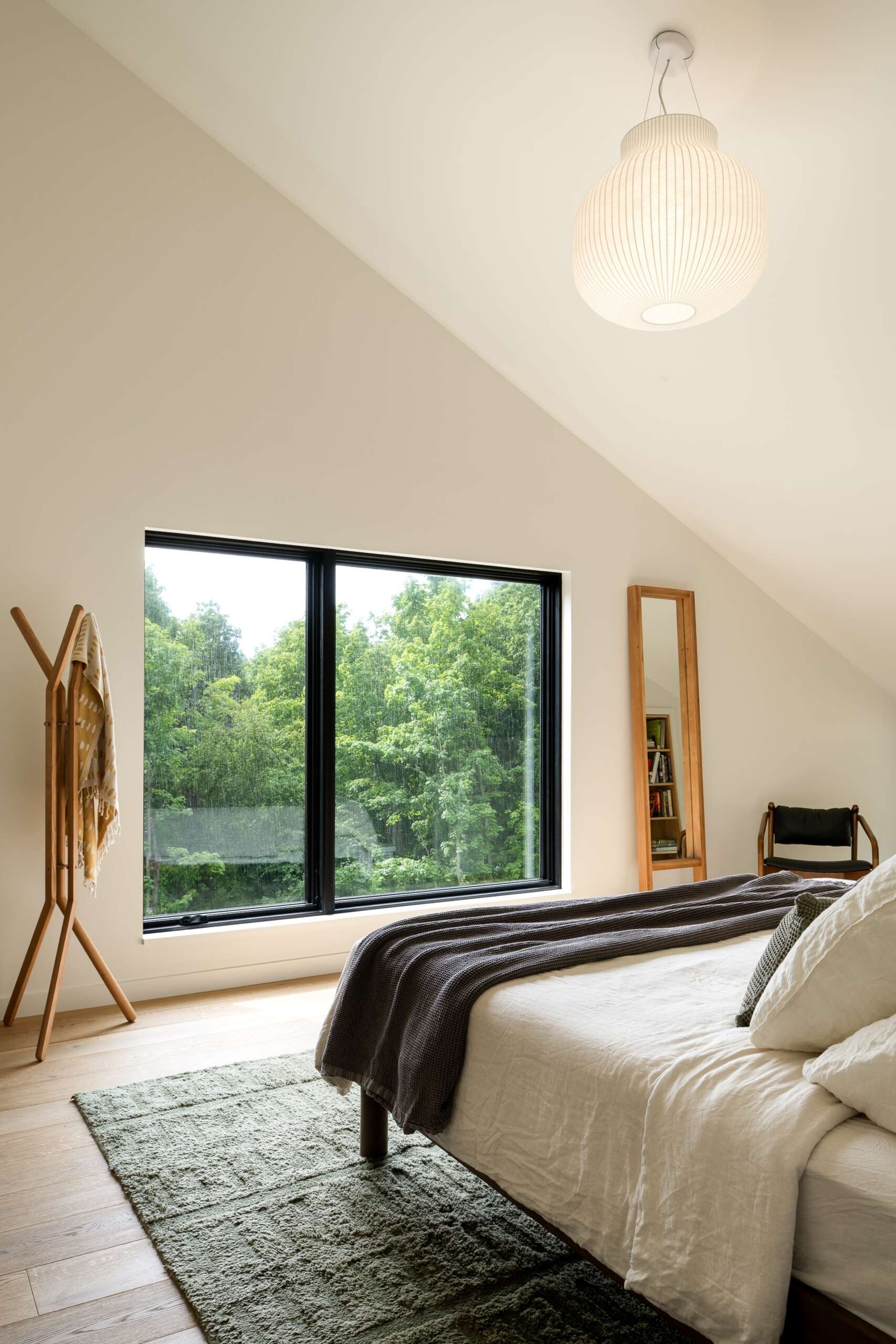 This primary bedroom moves away from the scale of the main gathering spaces, offering a more intimate interior within the larger house. Lighter wood and natural light continue the material palette used throughout the residence.

A nook within the bedroom has been transformed into a reading corner with a built-in bookshelf and a window.