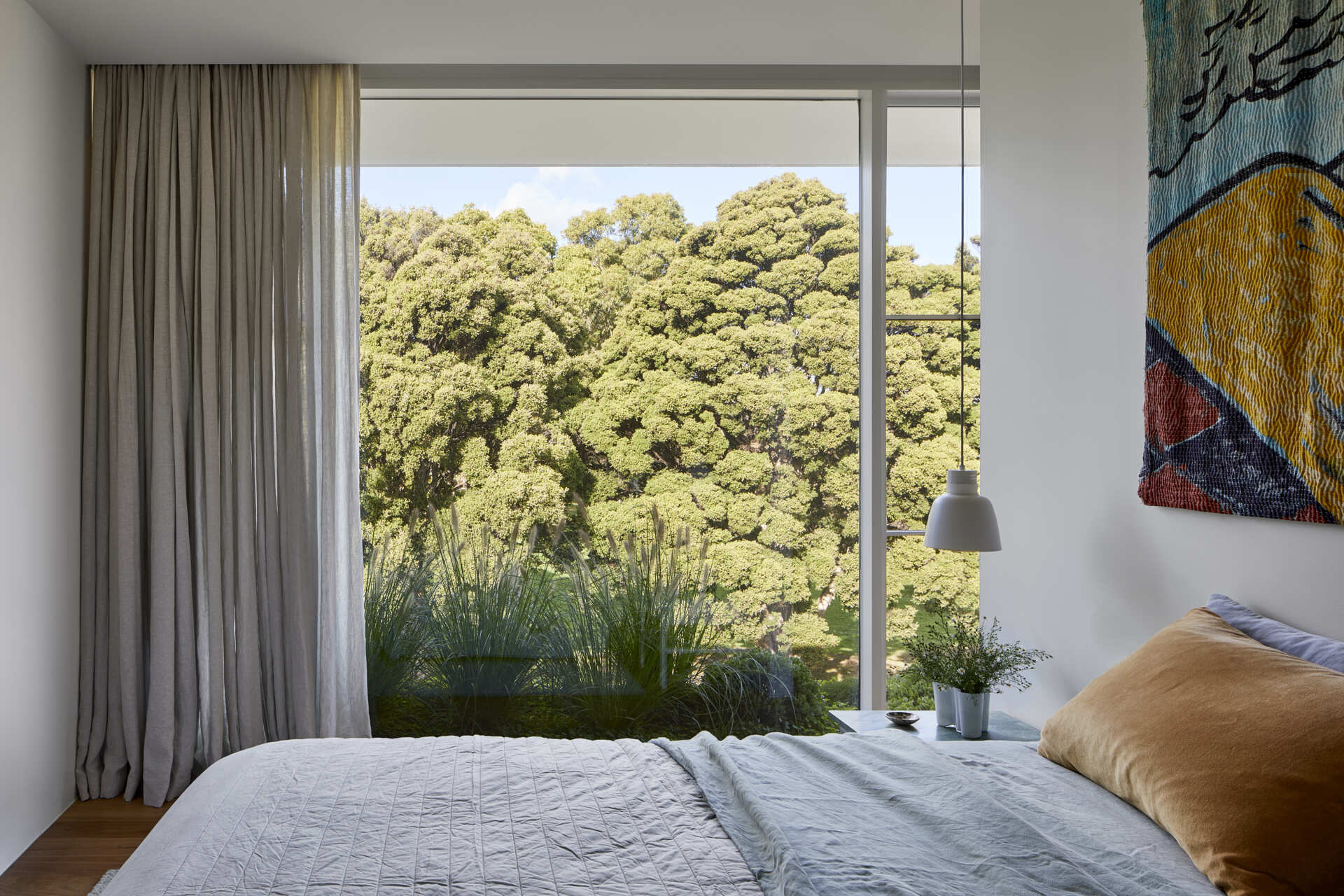 The main bedroom features a floor-to-ceiling window looking directly towards mature trees, and a wall of cabinetry with a green marble accent.