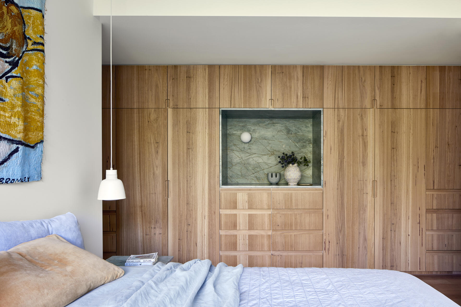 The main bedroom features a floor-to-ceiling window looking directly towards mature trees, and a wall of cabinetry with a green marble accent.