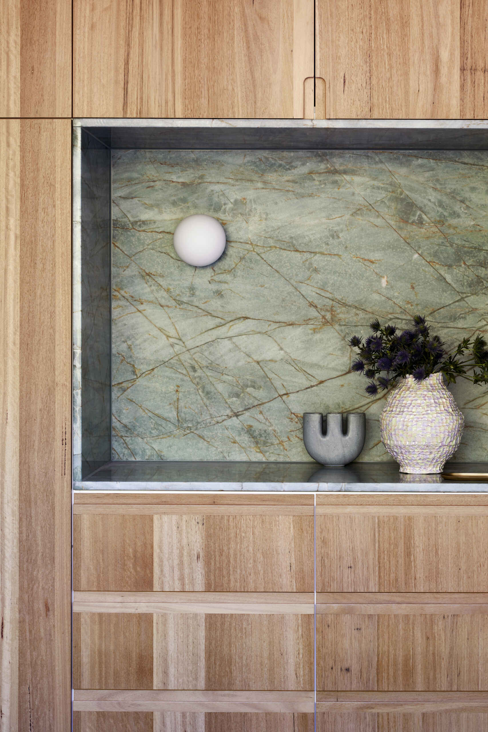 The main bedroom features a floor-to-ceiling window looking directly towards mature trees, and a wall of cabinetry with a green marble accent.
