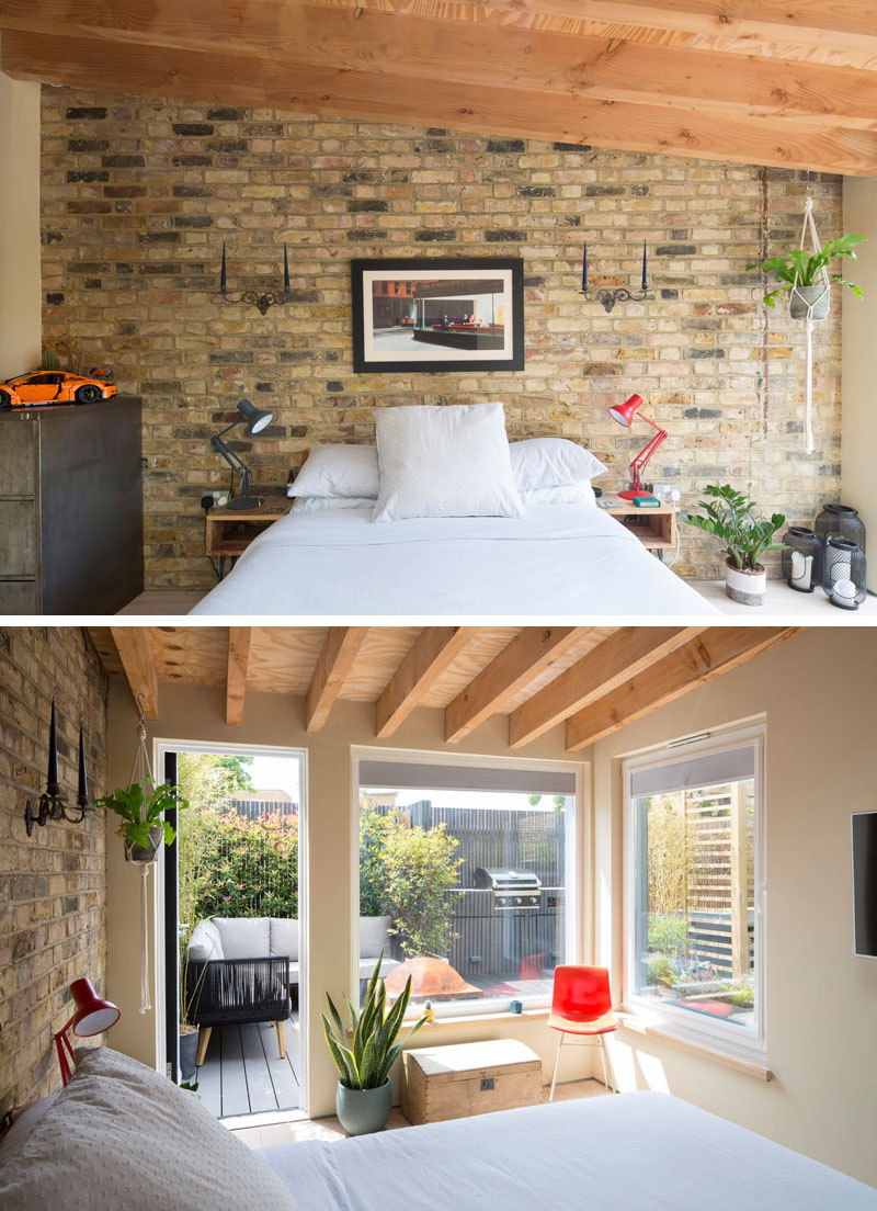 An exposed brick wall, timber beams and large windows give the new main bedroom in this London home a warm architectural character while framing views of the backyard.