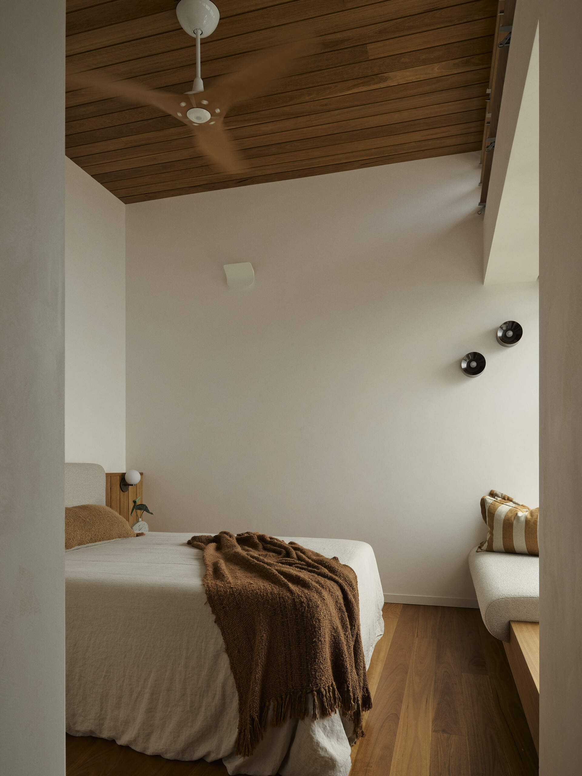 A cosy guest bedroom in this Byron Bay beach house features a built-in window bench, warm natural finishes and generous glazing that makes the most of the surrounding coastal views.
