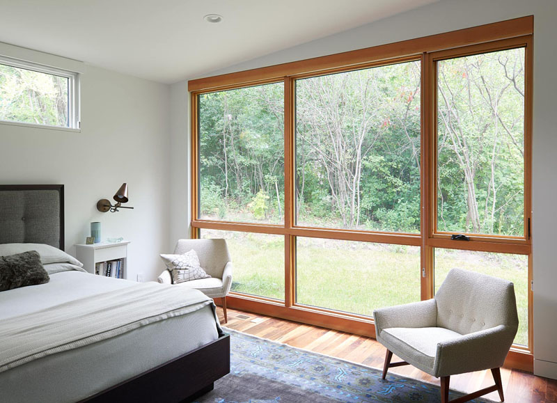 Large wood-framed windows become the focal point of this mostly white bedroom, adding warmth and views to the modern interior.