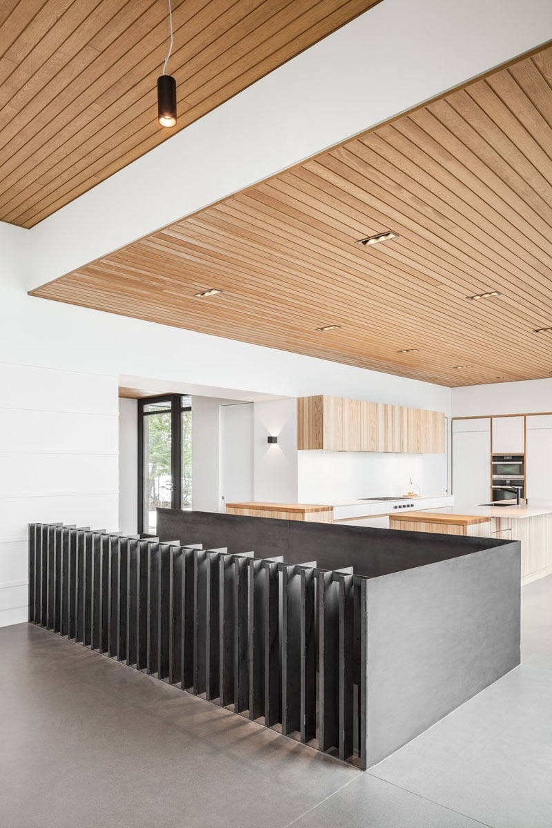 A steel stair railing separates the living room from the staircase leading down to the bedrooms and bathrooms, adding an industrial detail to the warm wood and concrete interior of this Québec house.