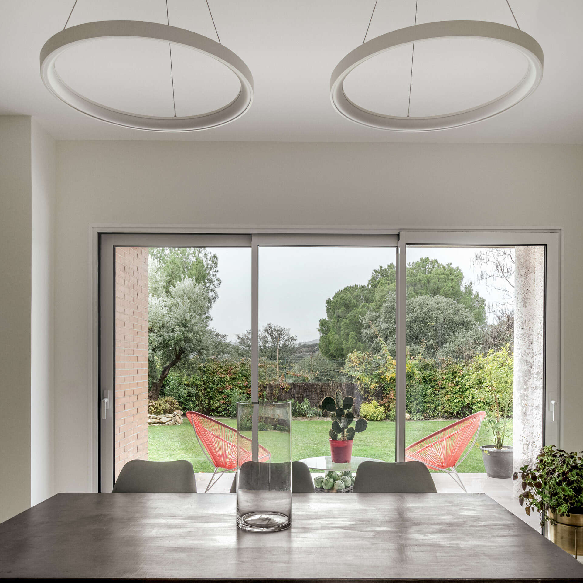 A long industrial-style dining table, Nordic chairs and garden views define the main dining area at the opposite end of this Madrid home.