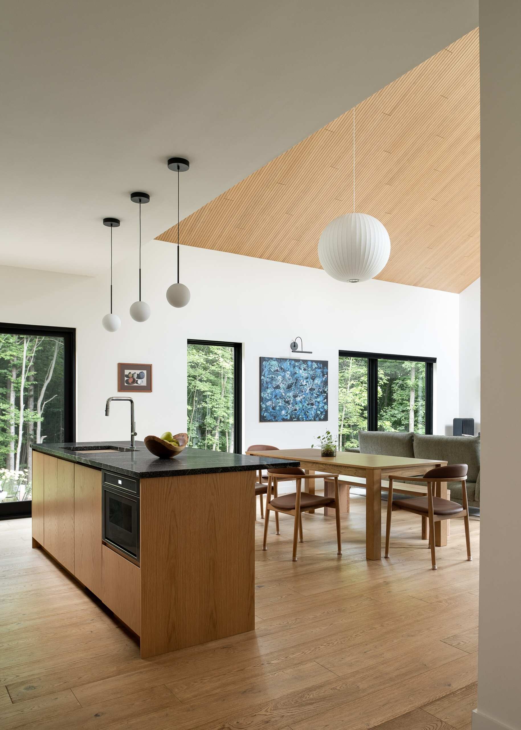 Explore the dining and kitchen spaces of this Vermont hillside home, featuring lofty ceilings, lighter wood finishes, natural light and views through the surrounding trees.
