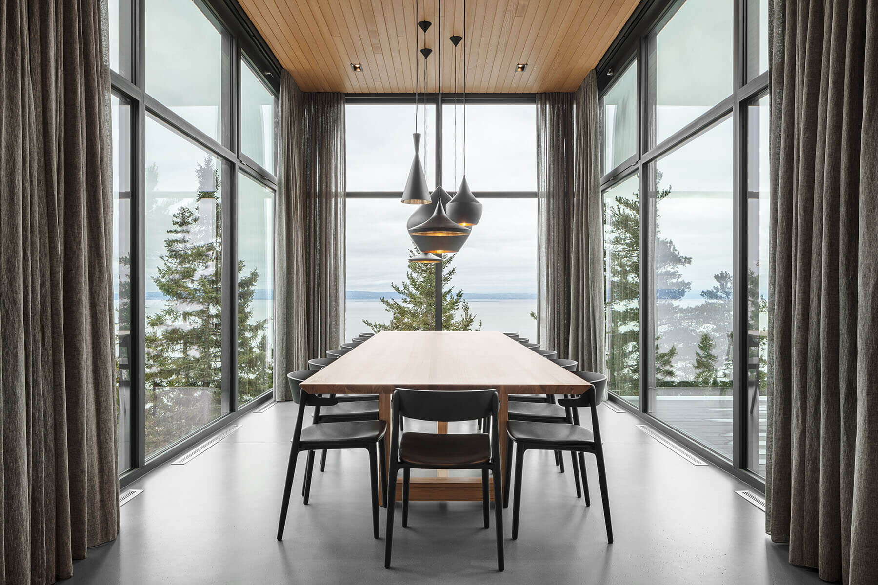 This glass-wrapped dining room extends away from the main house toward the horizon, with windows on three sides framing expansive views of the St. Lawrence River.