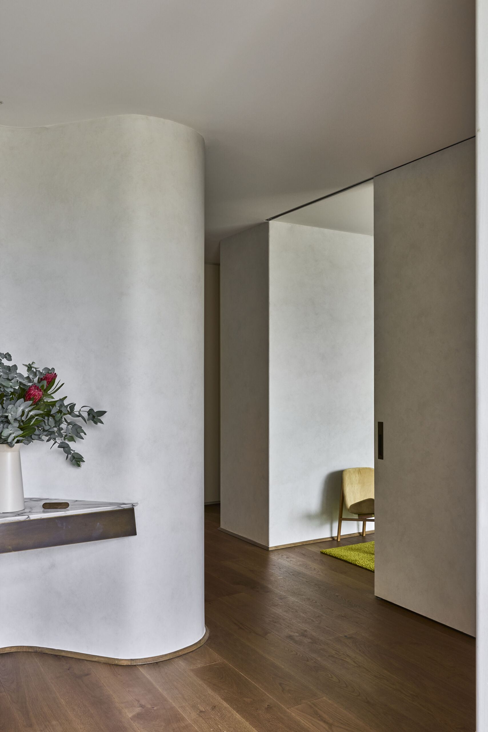 Step inside Sasso Nero through a sculptural entrance framed by vertical timber battens, dark charred cladding and lush planting. A curved ceiling opening brings natural light into the entryway.