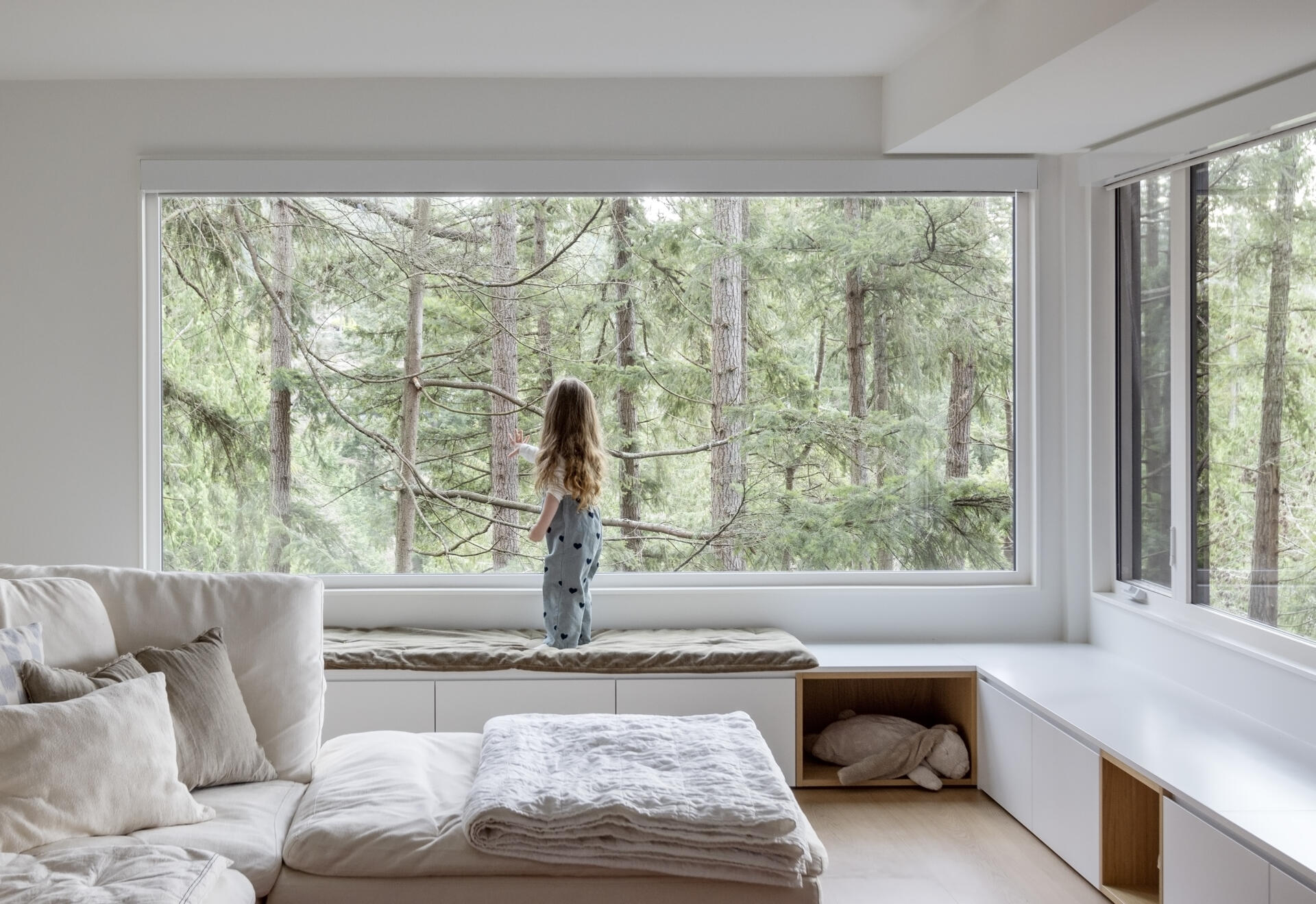 Enlarged windows, built-in shelving and storage benches transform the lower-level family room of this West Vancouver home into a bright space overlooking the surrounding trees.