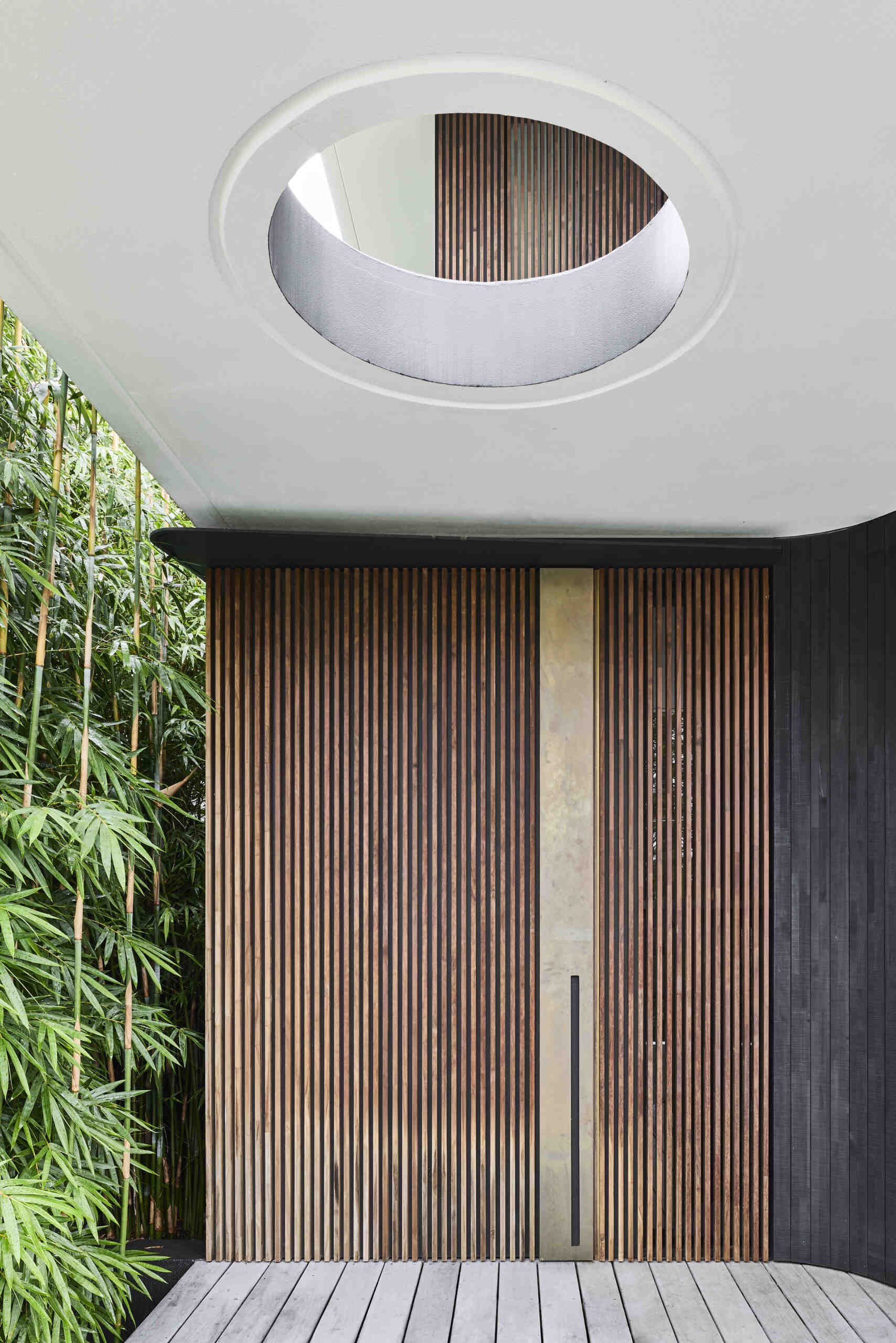 Step inside Sasso Nero through a sculptural entrance framed by vertical timber battens, dark charred cladding and lush planting. A curved ceiling opening brings natural light into the entryway.
