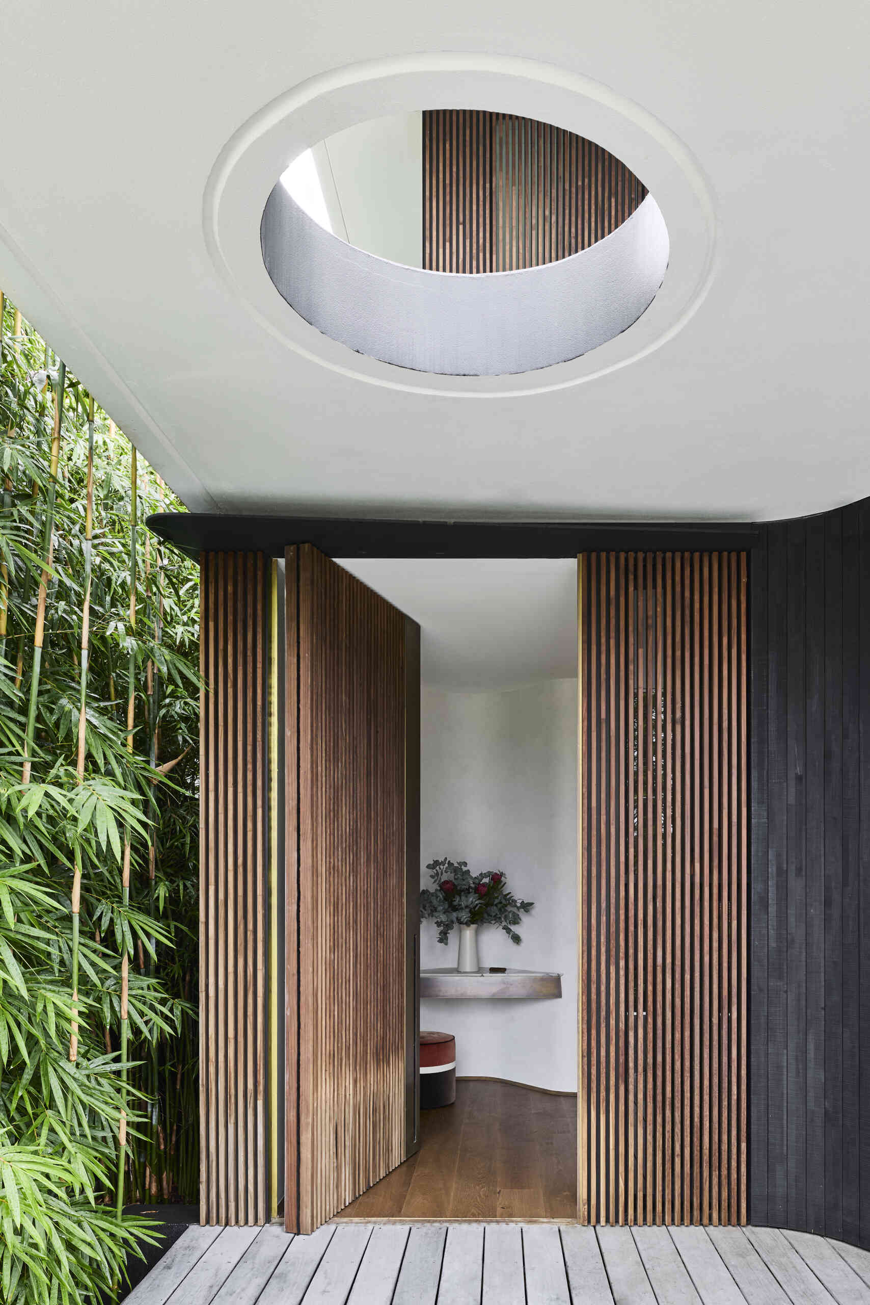 Step inside Sasso Nero through a sculptural entrance framed by vertical timber battens, dark charred cladding and lush planting. A curved ceiling opening brings natural light into the entryway.