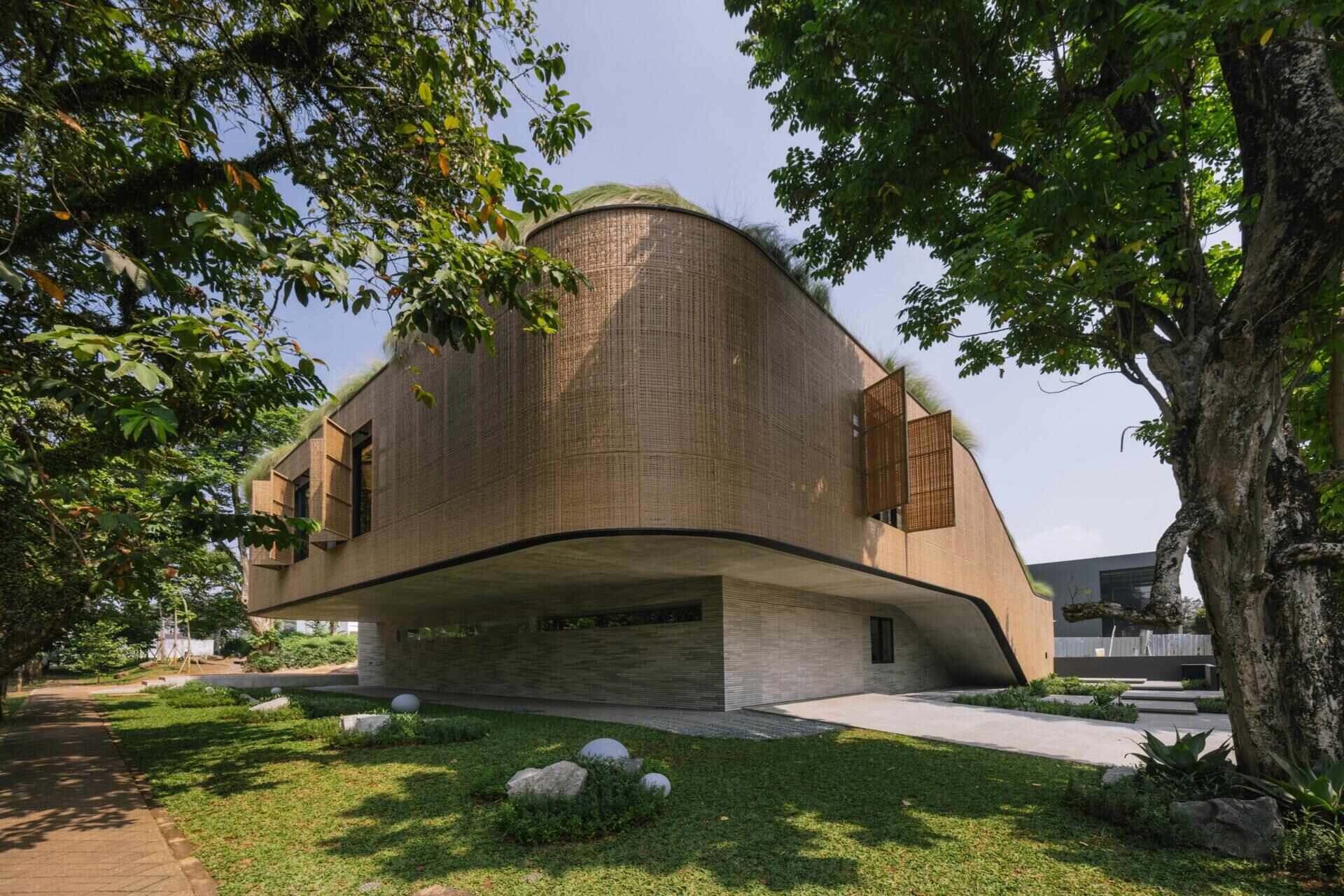 Explore the exterior of Split Mass Residence, where split architectural volumes, rounded corners, bamboo-textured concrete and woven recycled PET rattan screens shape this Indonesian home.