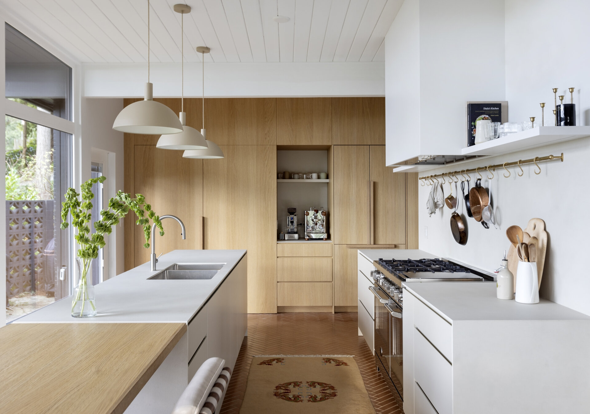 See how a 1961 mid-century kitchen was transformed with white oak cabinetry, a hidden pantry, coffee station, breakfast bar and oversized island, creating a warm and functional space for cooking and family gatherings.