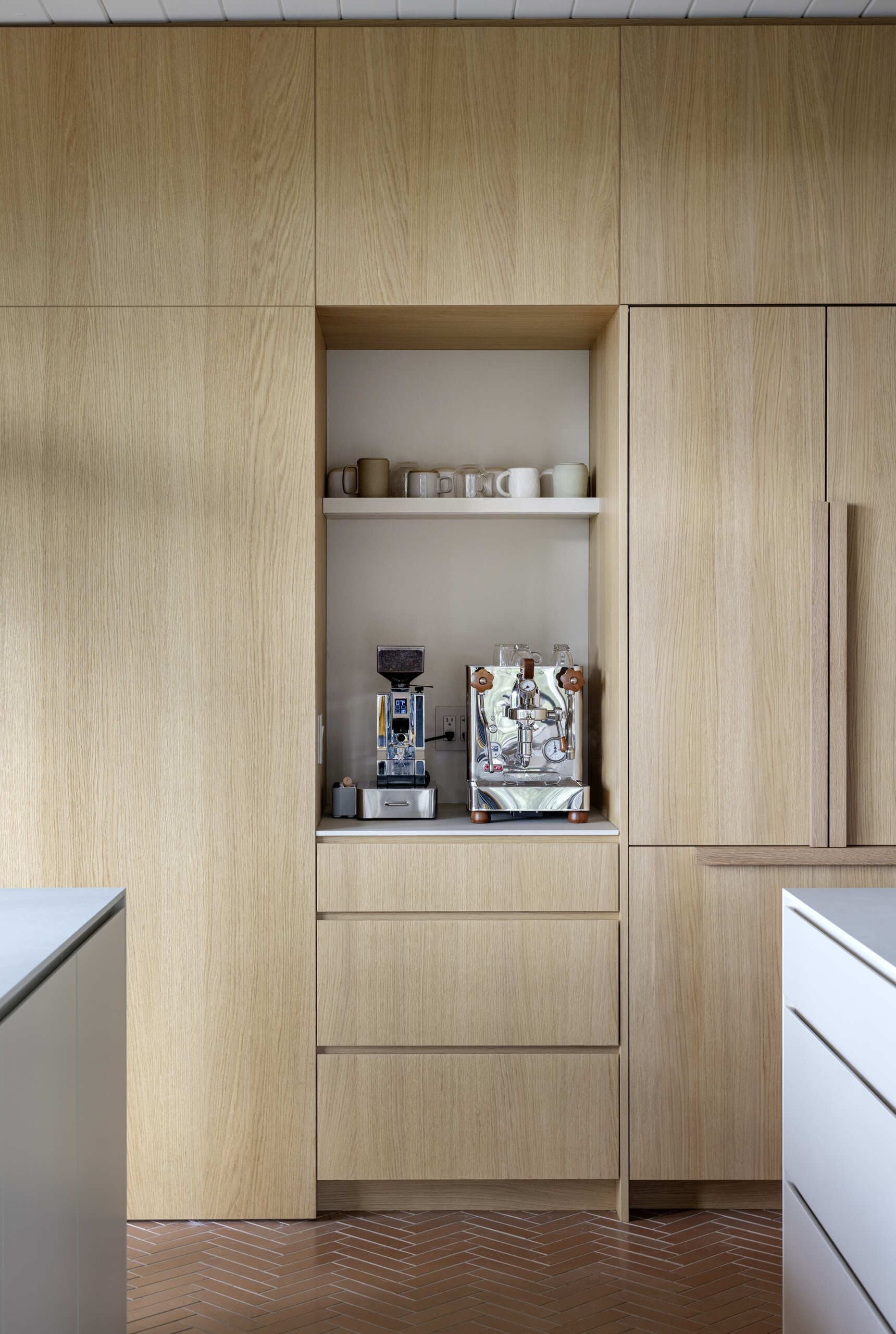 See how a 1961 mid-century kitchen was transformed with white oak cabinetry, a hidden pantry, coffee station, breakfast bar and oversized island, creating a warm and functional space for cooking and family gatherings.