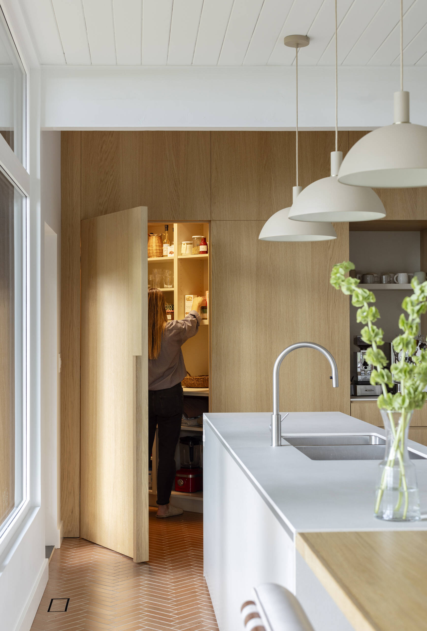 See how a 1961 mid-century kitchen was transformed with white oak cabinetry, a hidden pantry, coffee station, breakfast bar and oversized island, creating a warm and functional space for cooking and family gatherings.