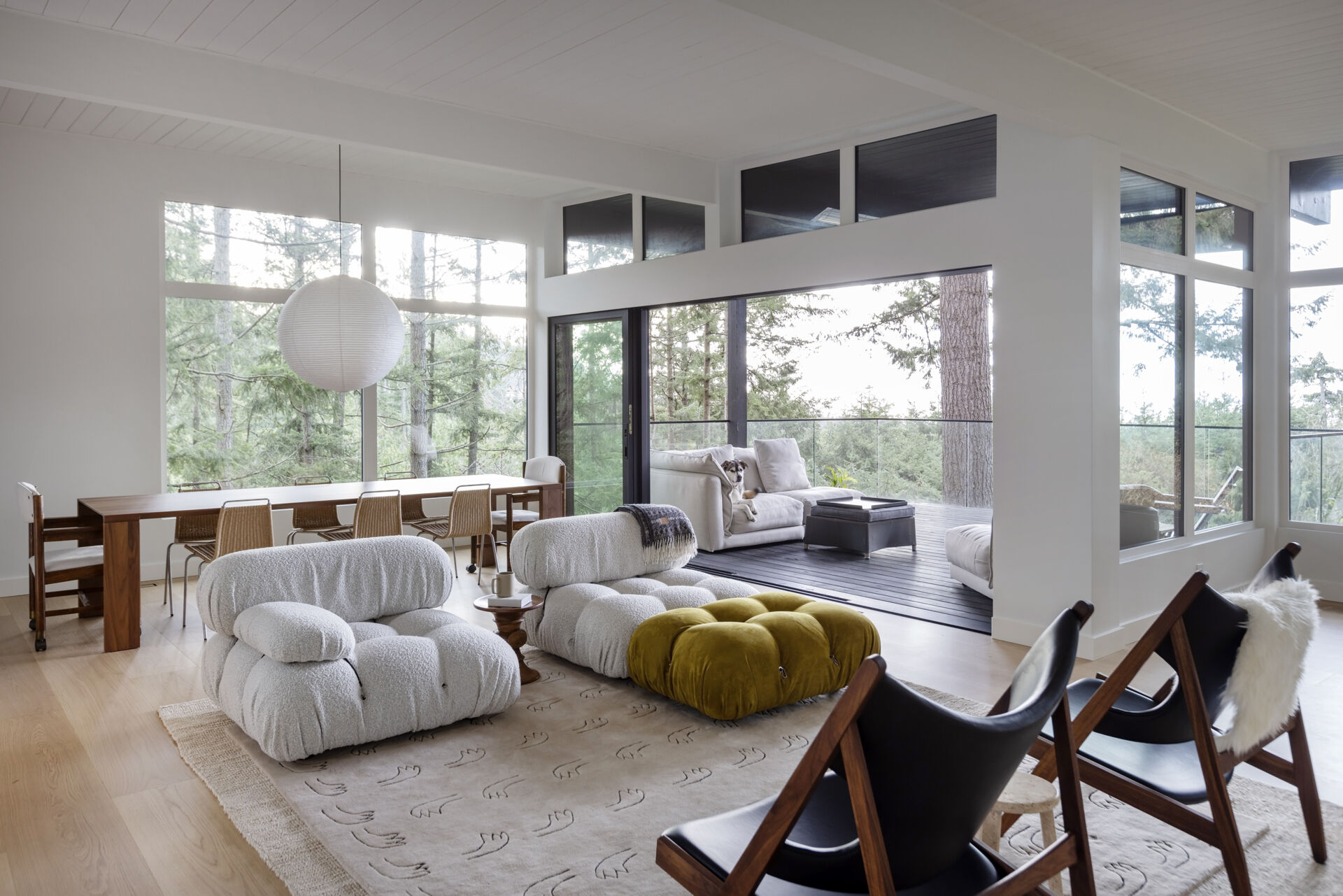 Explore the open living and dining spaces of this West Vancouver mid-century home, featuring an original brick wood-burning fireplace, upgraded windows, forest and ocean views, and large glass doors opening onto the deck.