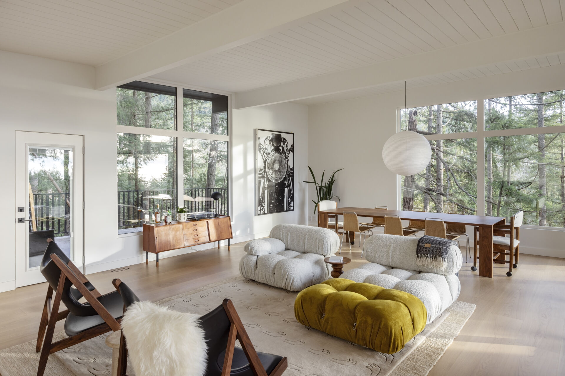 Explore the open living and dining spaces of this West Vancouver mid-century home, featuring an original brick wood-burning fireplace, upgraded windows, forest and ocean views, and large glass doors opening onto the deck.