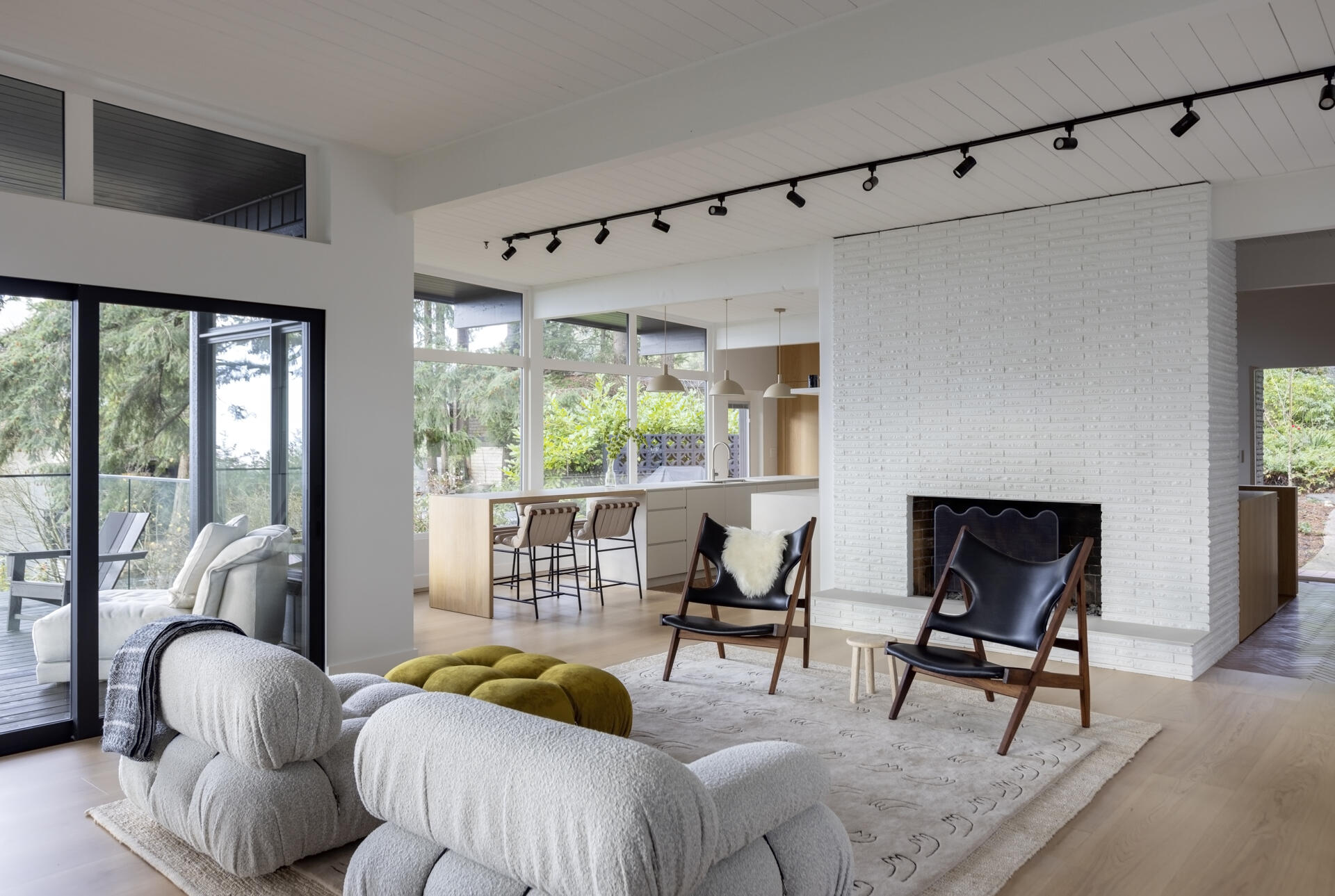 Explore the open living and dining spaces of this West Vancouver mid-century home, featuring an original brick wood-burning fireplace, upgraded windows, forest and ocean views, and large glass doors opening onto the deck.