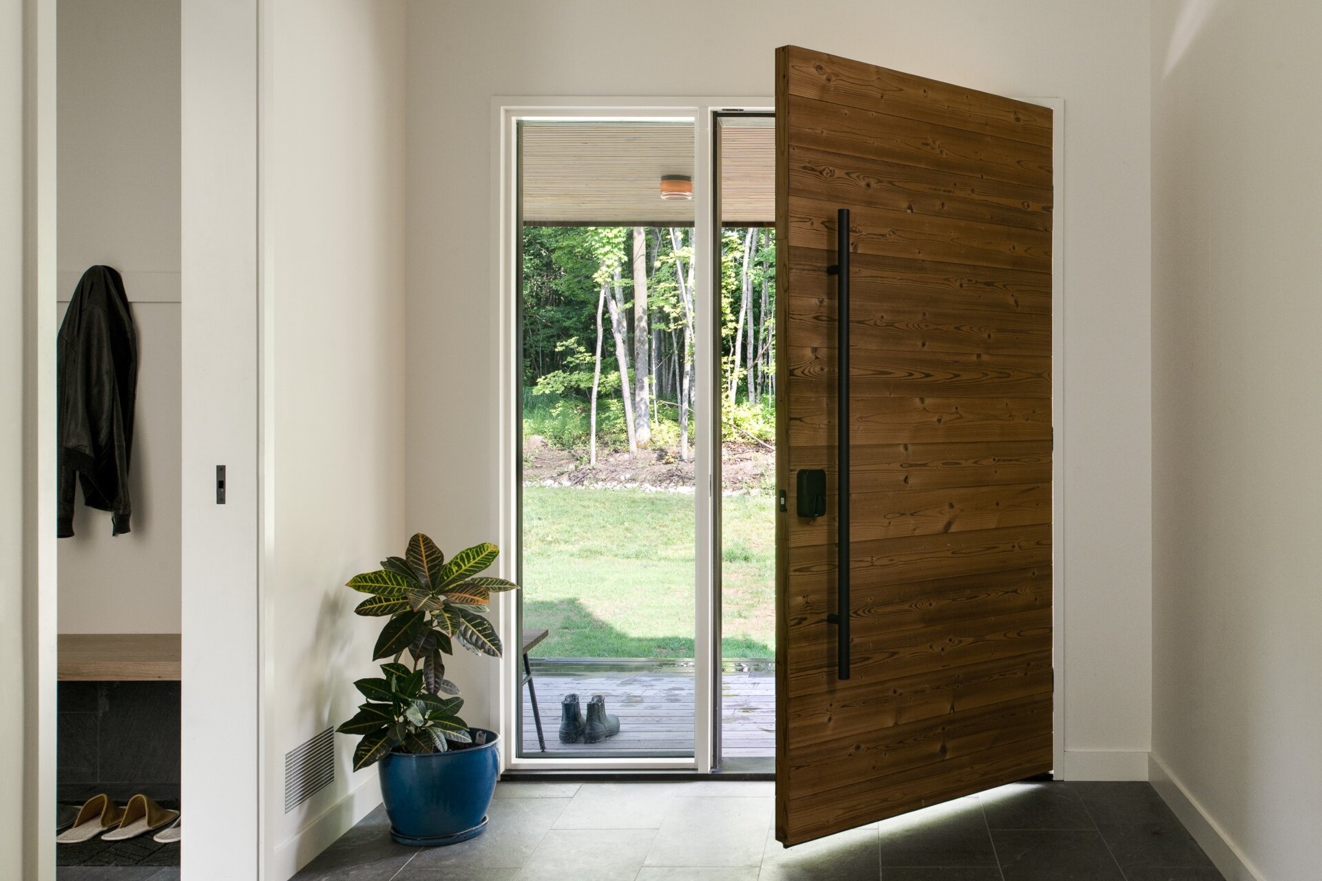The entryway begins the transition from the dark exterior into the lighter interior. The material palette becomes brighter as you move inside, with natural wood and daylight replacing the deep tones of the charred cedar outside. Just of the entrance, a built-in couch adds a cozy and practical element.
