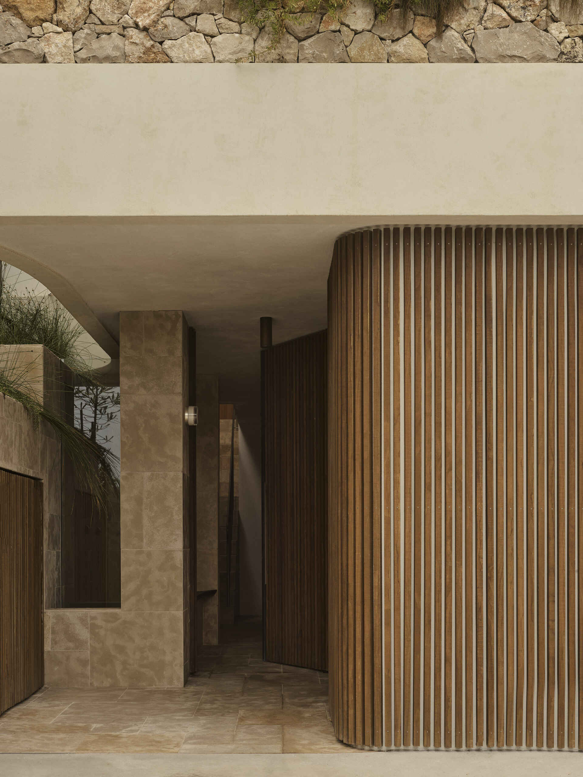 The arrival sequence begins beside the garage, where the architecture transitions into the stepped form of the property. The use of limestone helps tie the lower portion of the home to the rocky landscape, while the elevated gardens bring greenery onto the different levels.