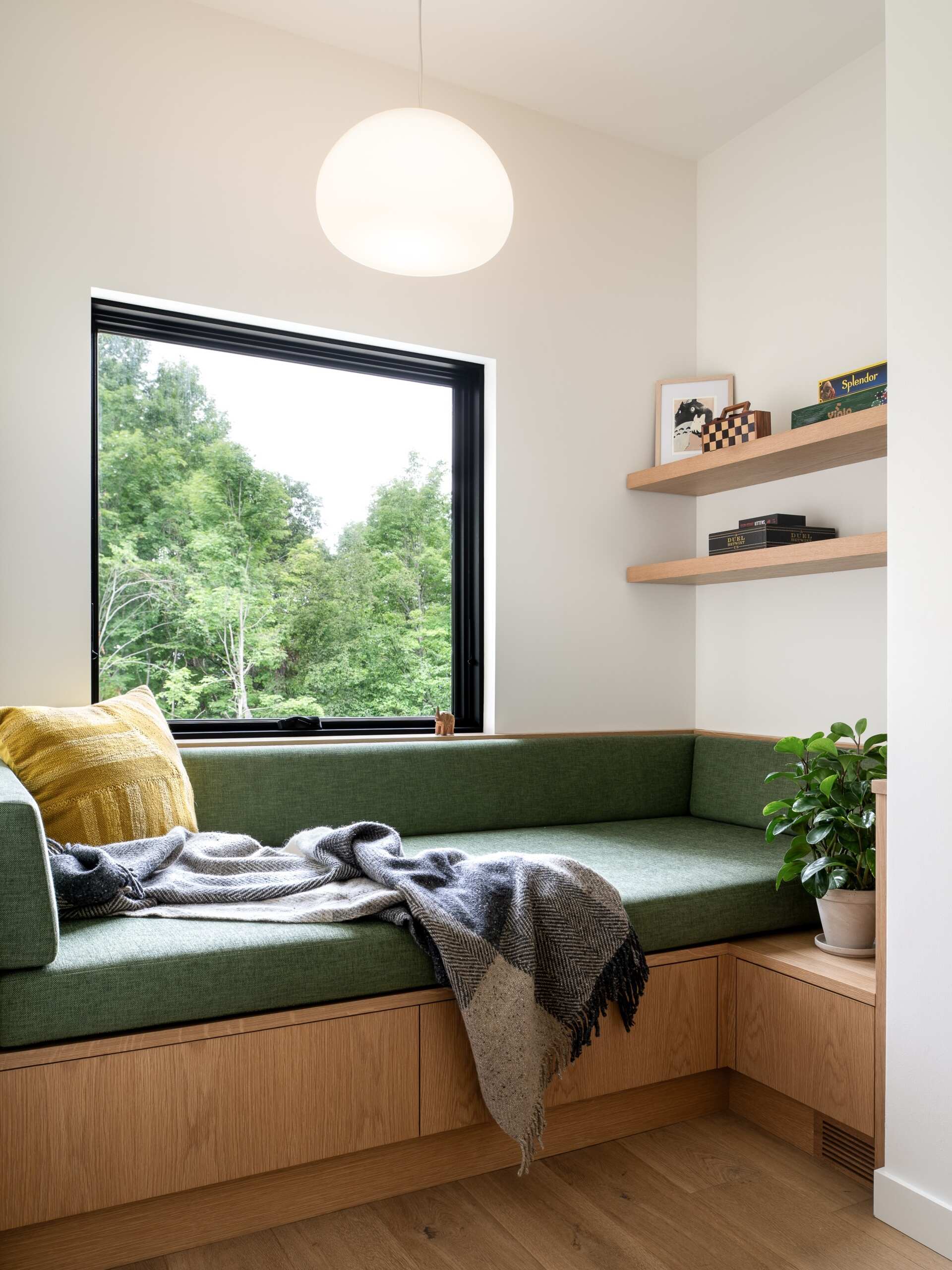 The entryway begins the transition from the dark exterior into the lighter interior. The material palette becomes brighter as you move inside, with natural wood and daylight replacing the deep tones of the charred cedar outside. Just of the entrance, a built-in couch adds a cozy and practical element.