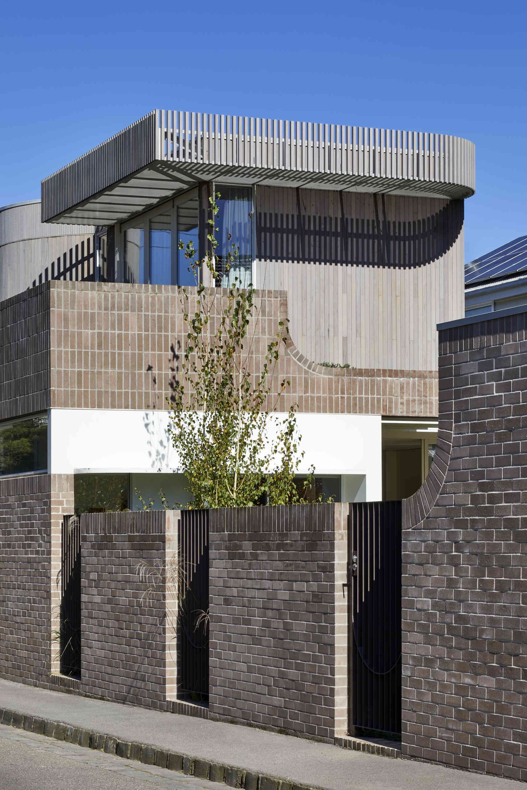 Warm Bowral brick and Blackbutt timber give this sculptural Clifton Hill extension an earthy exterior, while curved walls soften its contemporary form.