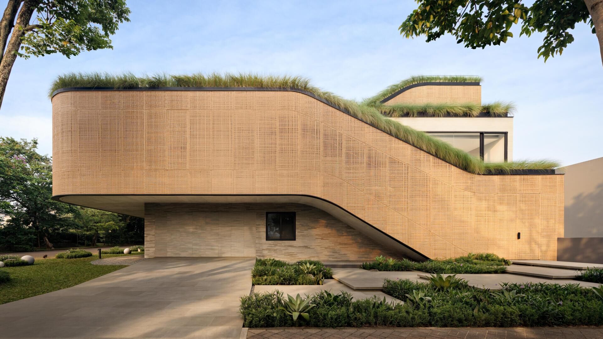 Explore the exterior of Split Mass Residence, where split architectural volumes, rounded corners, bamboo-textured concrete and woven recycled PET rattan screens shape this Indonesian home.