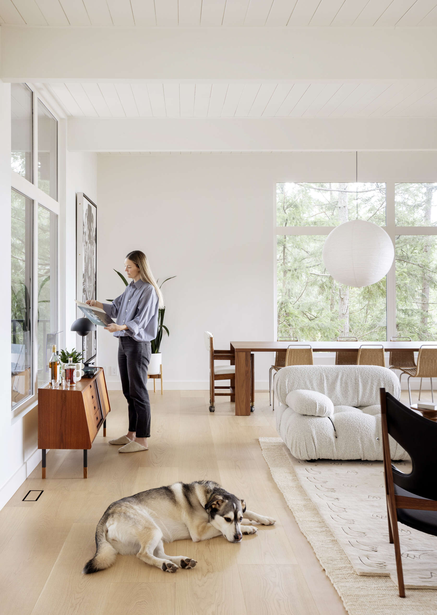 Explore the open living and dining spaces of this West Vancouver mid-century home, featuring an original brick wood-burning fireplace, upgraded windows, forest and ocean views, and large glass doors opening onto the deck.