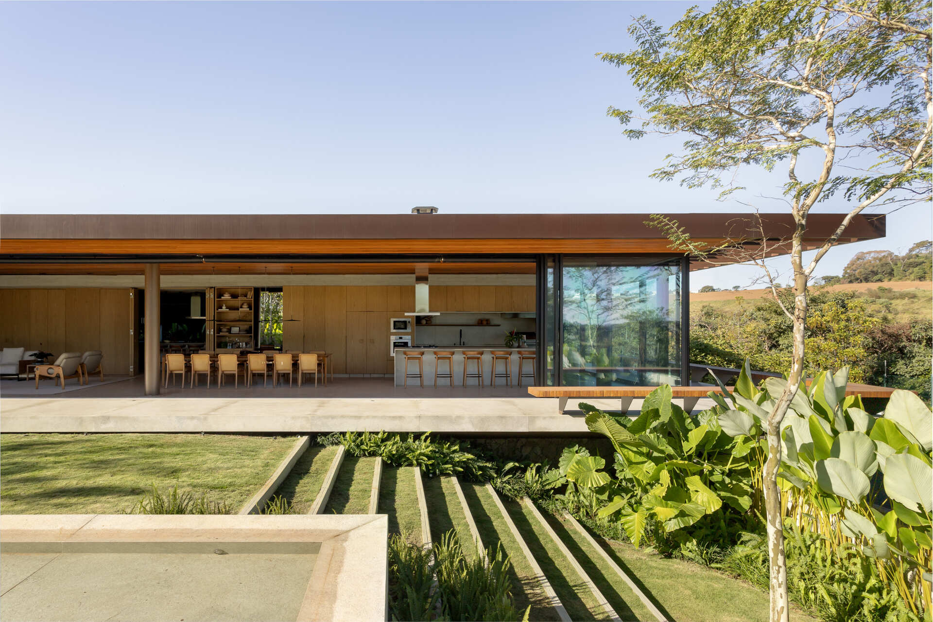The rectangular pool at Casa da Mata sits among tall palms, broad green leaves, a simple lawn and pale concrete edges, with a textured stone boundary wall creating a private tropical setting.