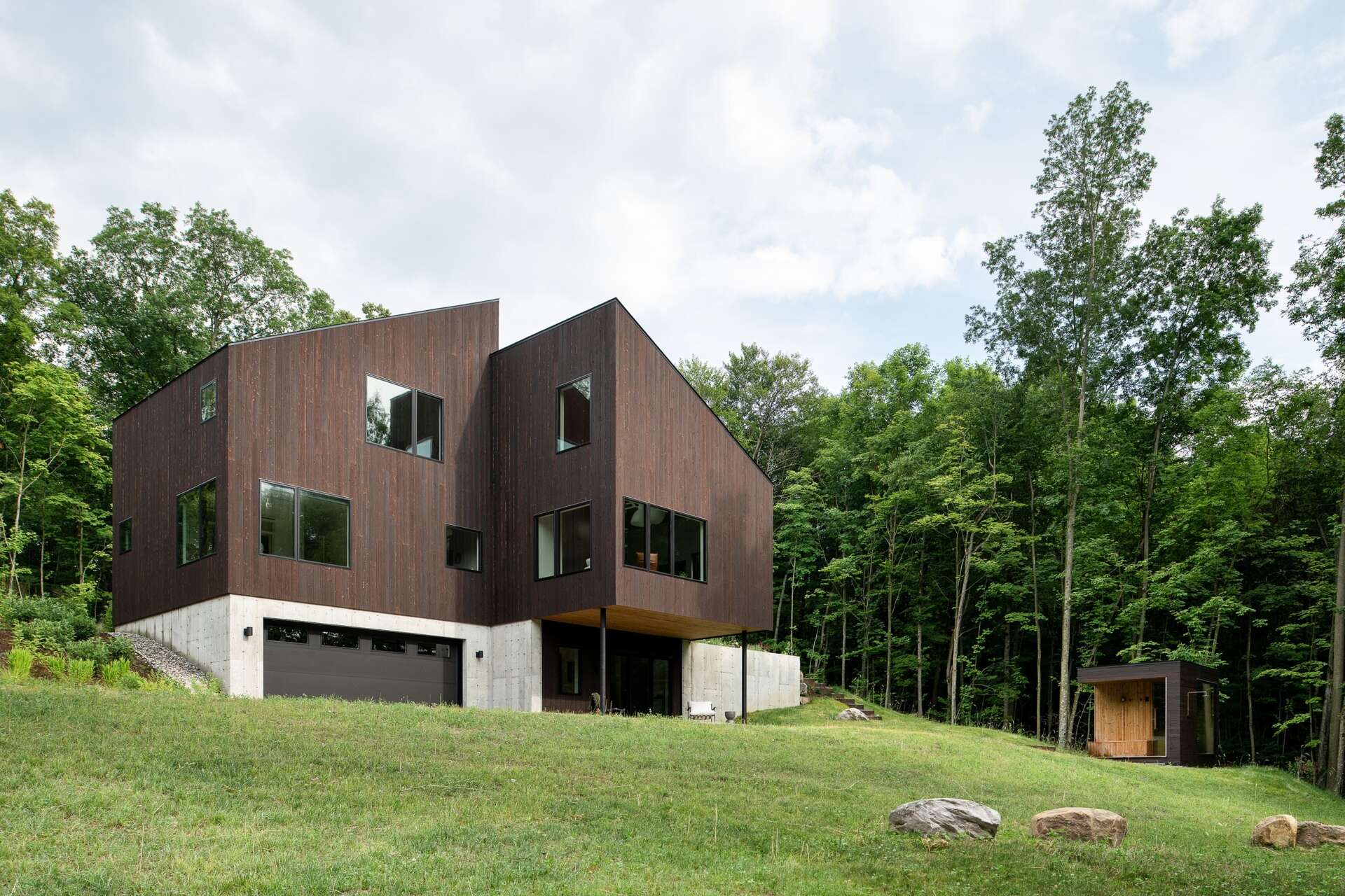 Discover the Milo House in Cornwall, Vermont, where irregular architectural volumes and dark Gendai® yakisugi siding give this hillside home a bark-like appearance among the trees.
