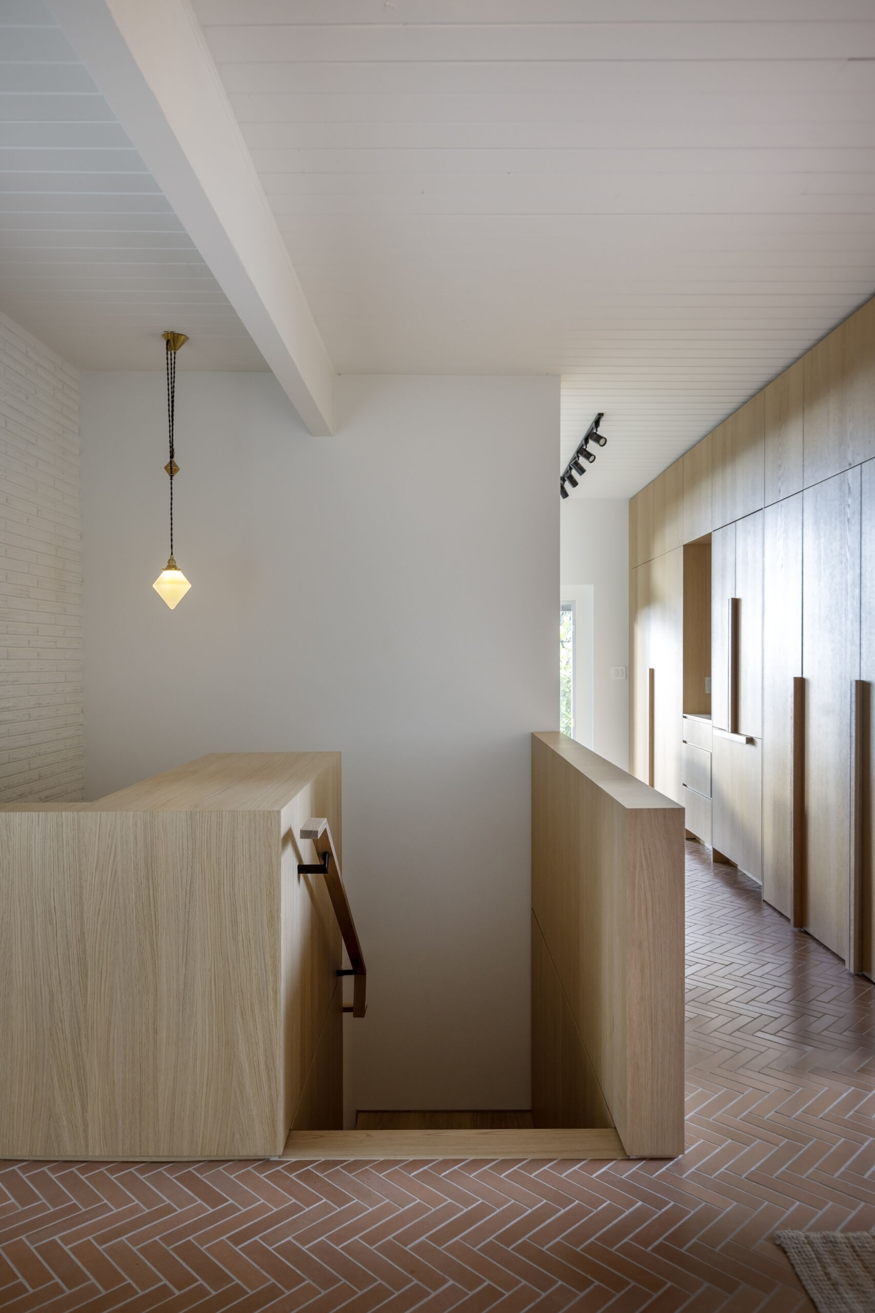 A dated spiral staircase was replaced with a squared-off stairwell wrapped in warm white oak panelling, creating a brighter transition between the main and lower levels of this renovated home.